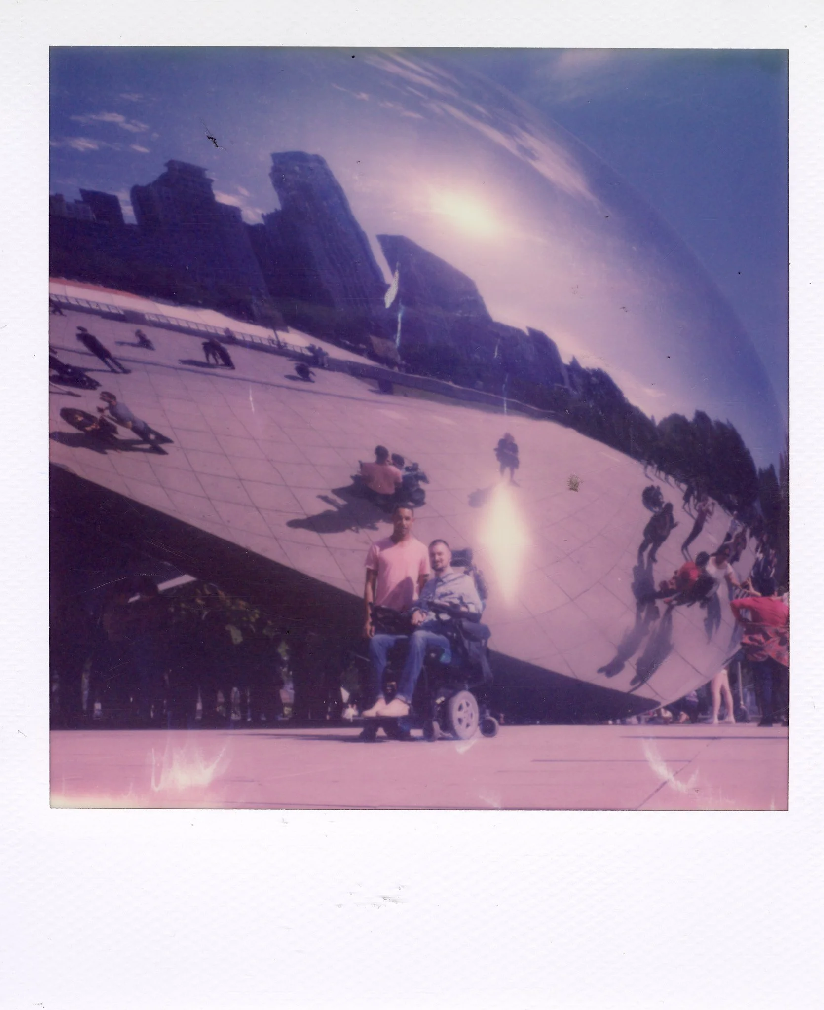 People taking a photo of the Cloud Gate sculpture in Millennium Park, Chicago, reflected on its shiny, curved surface.