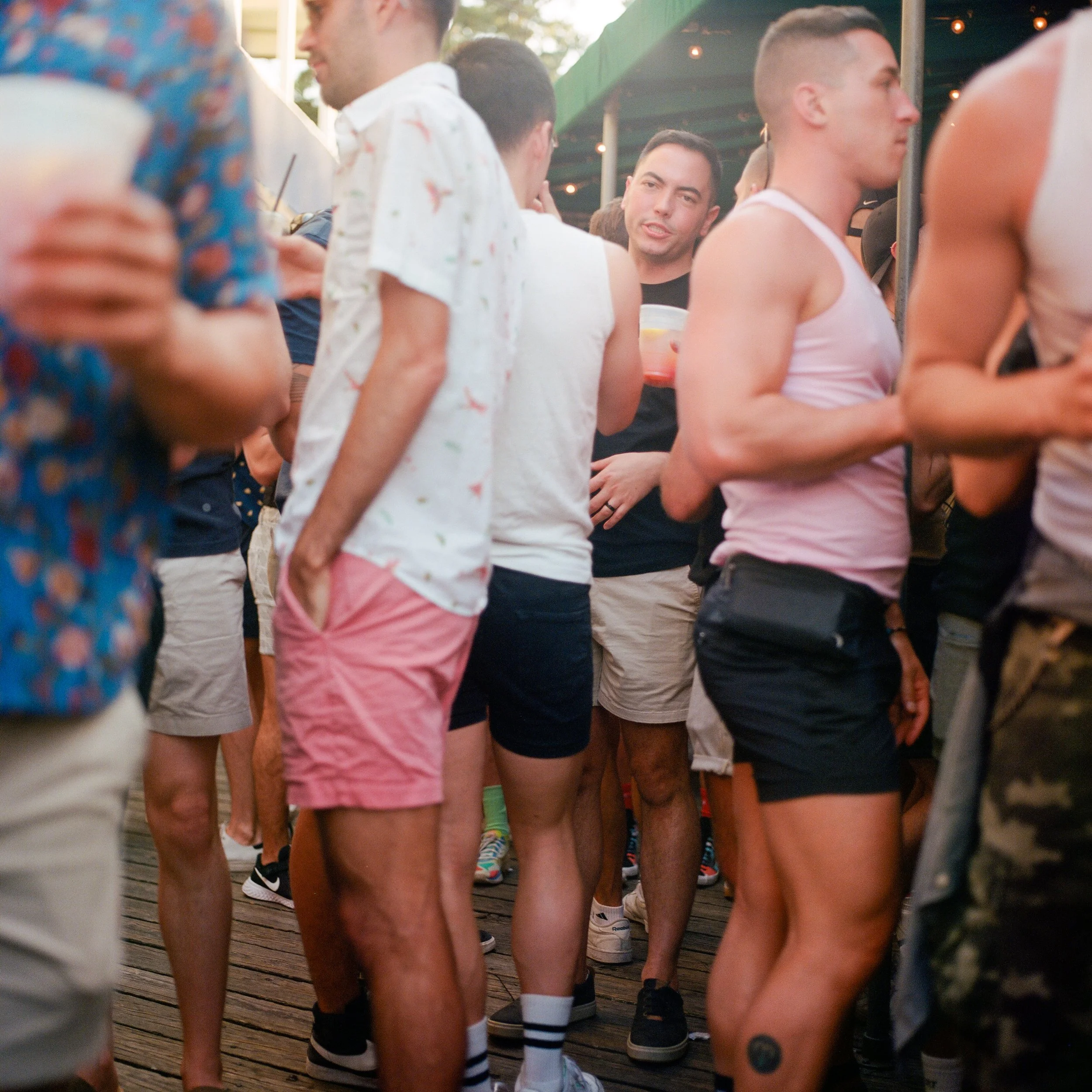 People gathered at an outdoor event, some holding drinks, wearing casual summer clothes.
