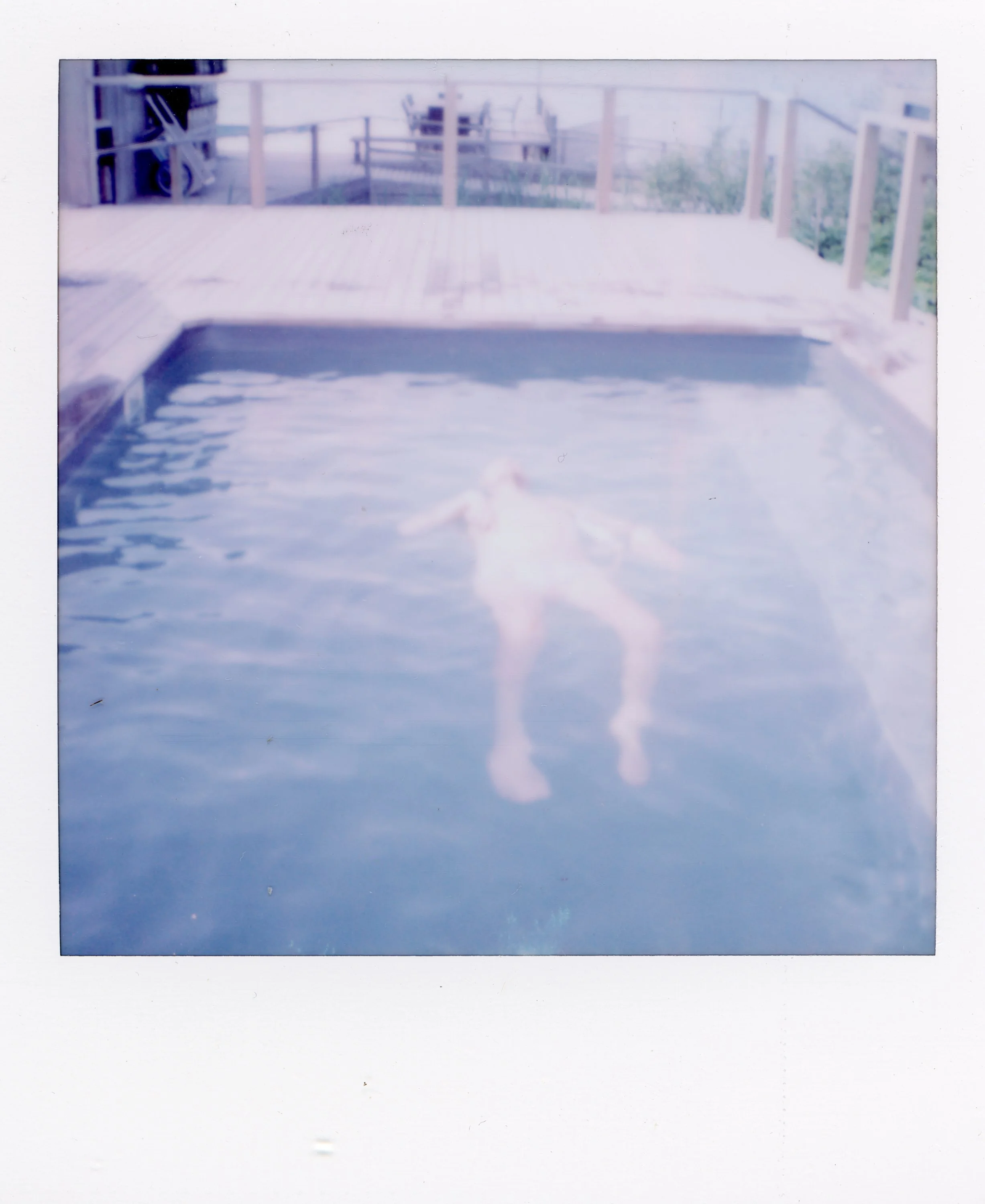 A person swimming in an outdoor pool with a wooden deck and railing, blurred and overexposed.