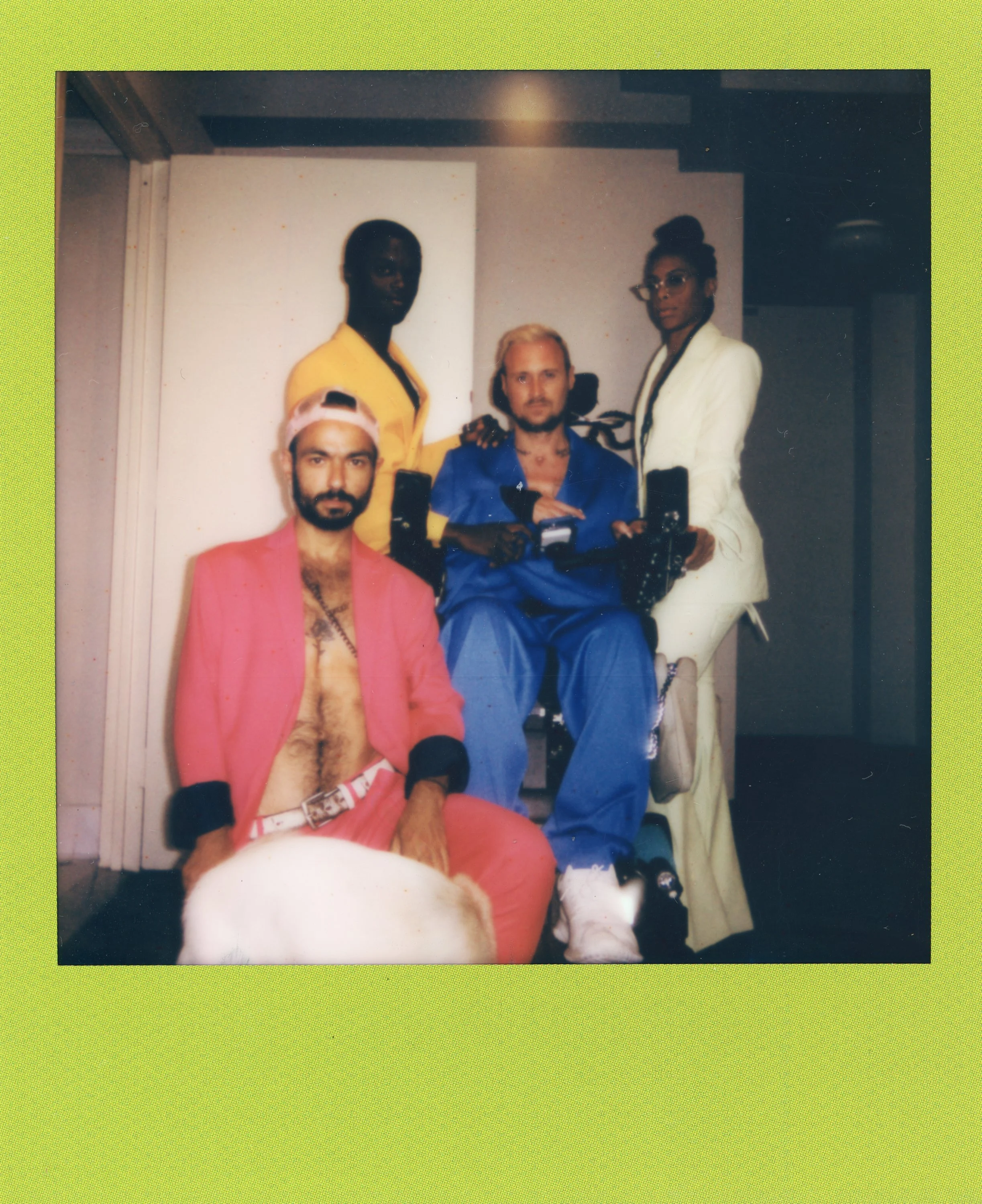 Four diverse individuals posing together indoors, with one in a wheelchair and a dog sitting in front, all dressed in colorful clothing.