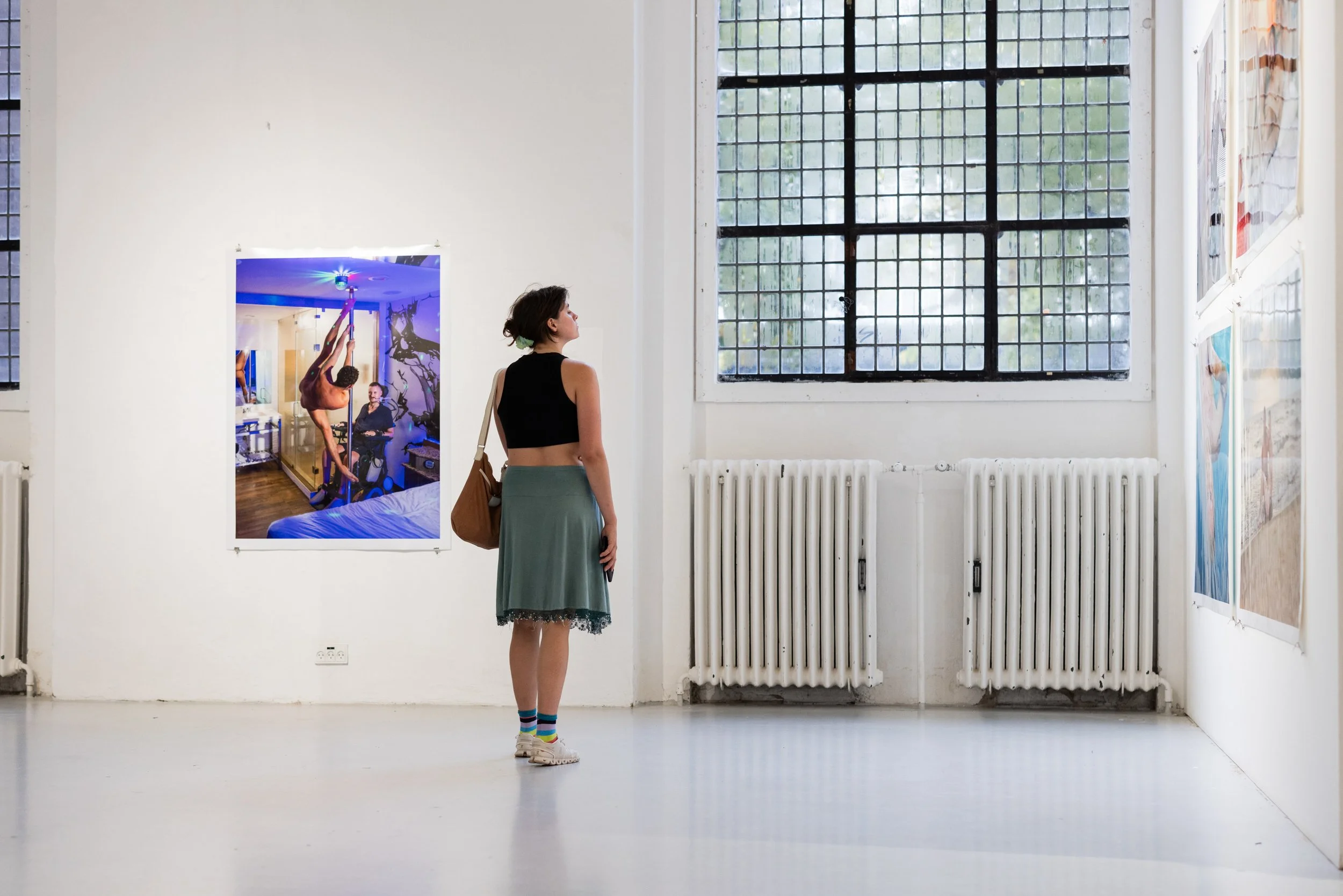 A woman viewing artwork in a gallery with white walls, large windows, and photos displayed.