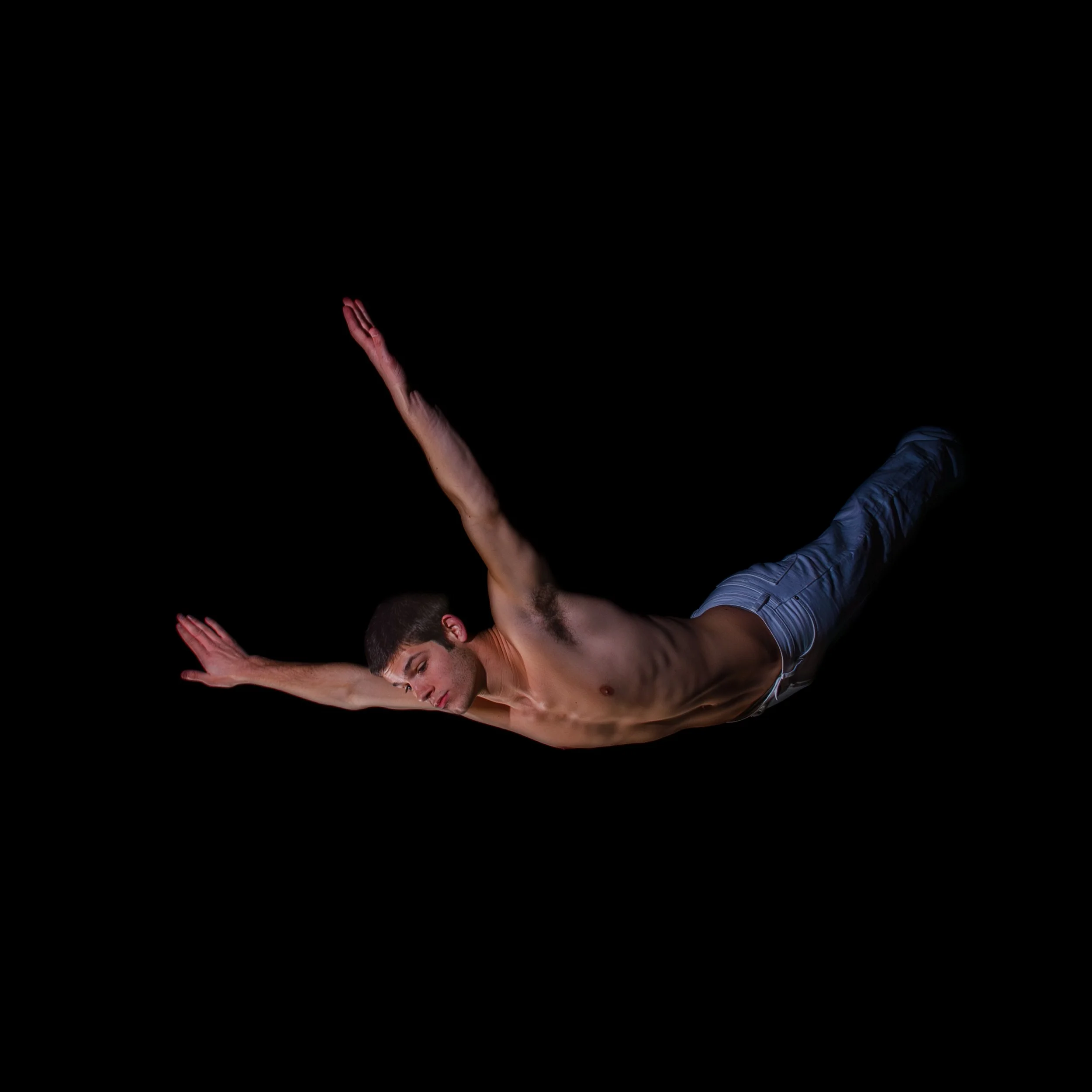 A shirtless man with jeans flying through the air against a black background, arms outstretched and eyes closed.