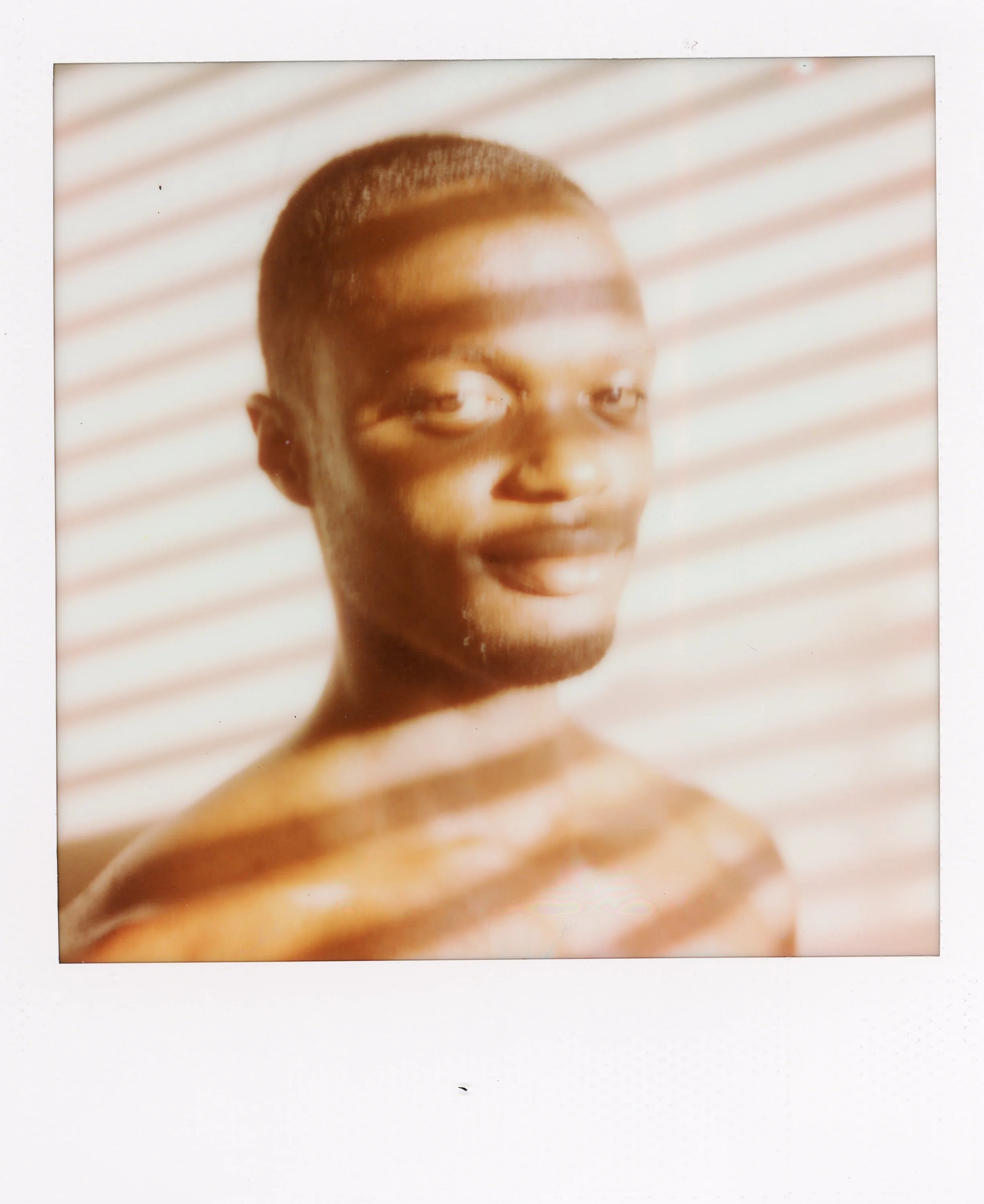 A portrait of a young person with short hair, smiling softly, with light and shadow stripes across their face and shoulders.