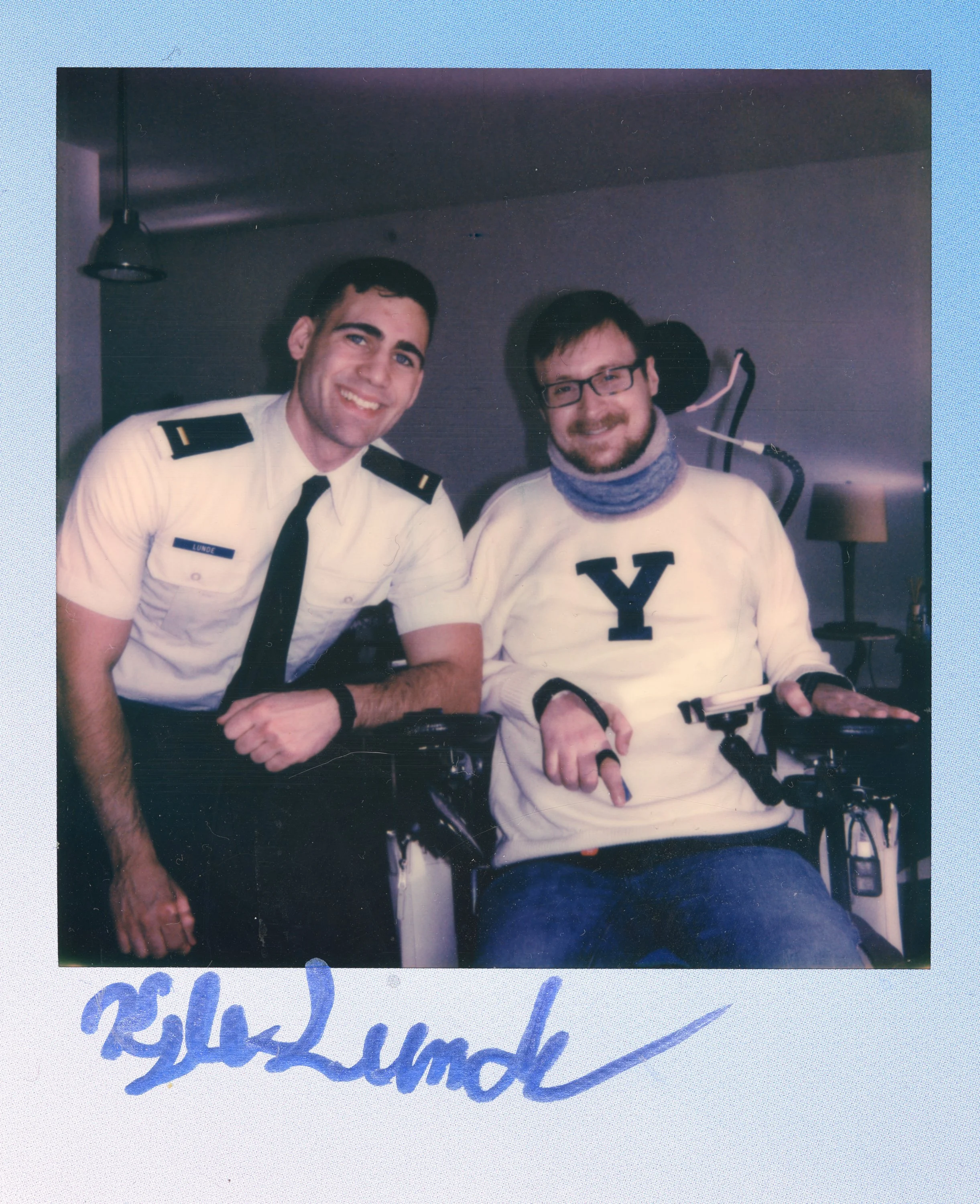 Two smiling men, one in a Yale sweatshirt and the other in a U.S. Coast Guard uniform, pose together indoors. The man in uniform has a name tag that reads 'Lunde.' The photo has a handwritten signature at the bottom.