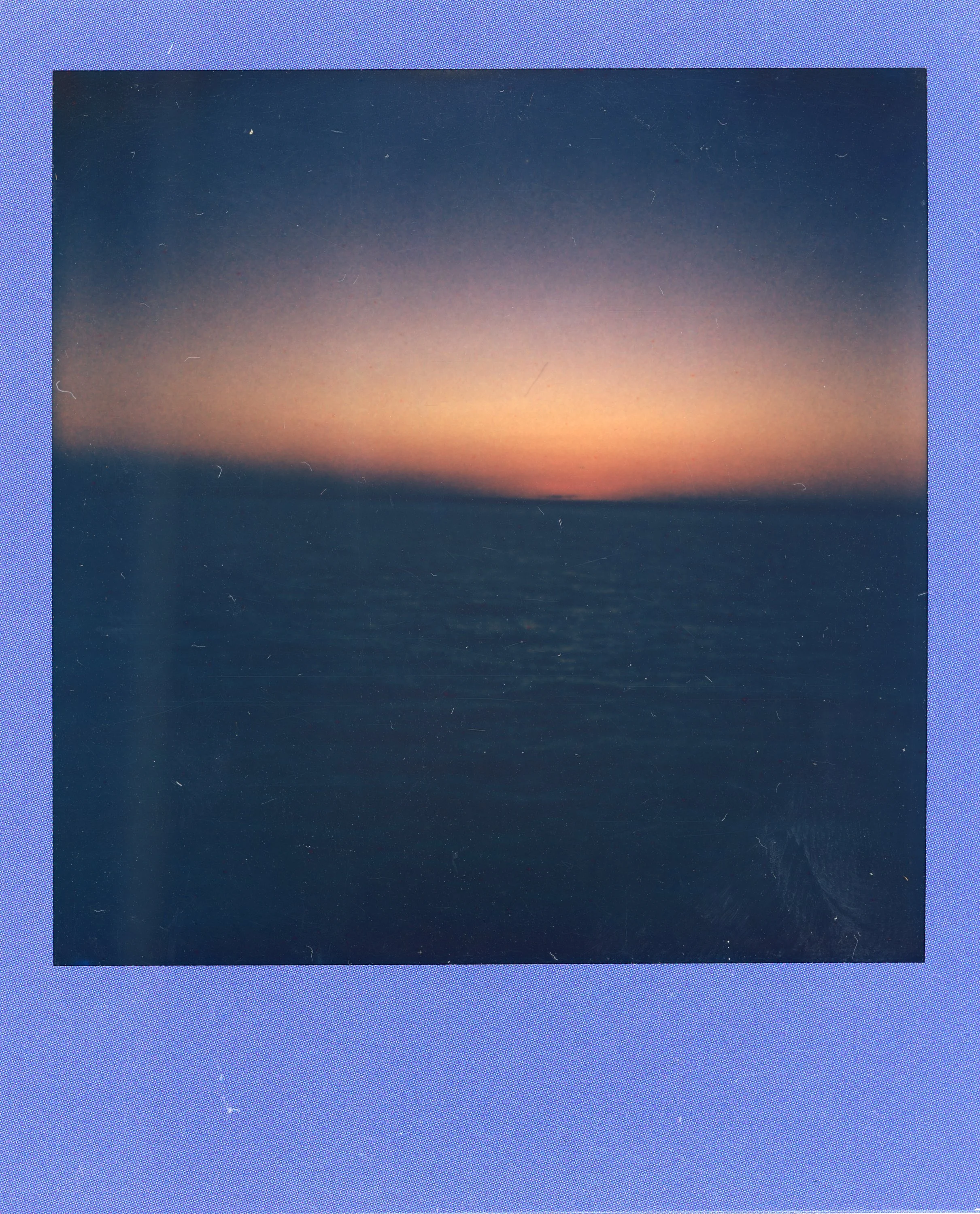 A sunset or sunrise over a calm ocean, with the sky transitioning from light pink near the horizon to dark blue at the top.