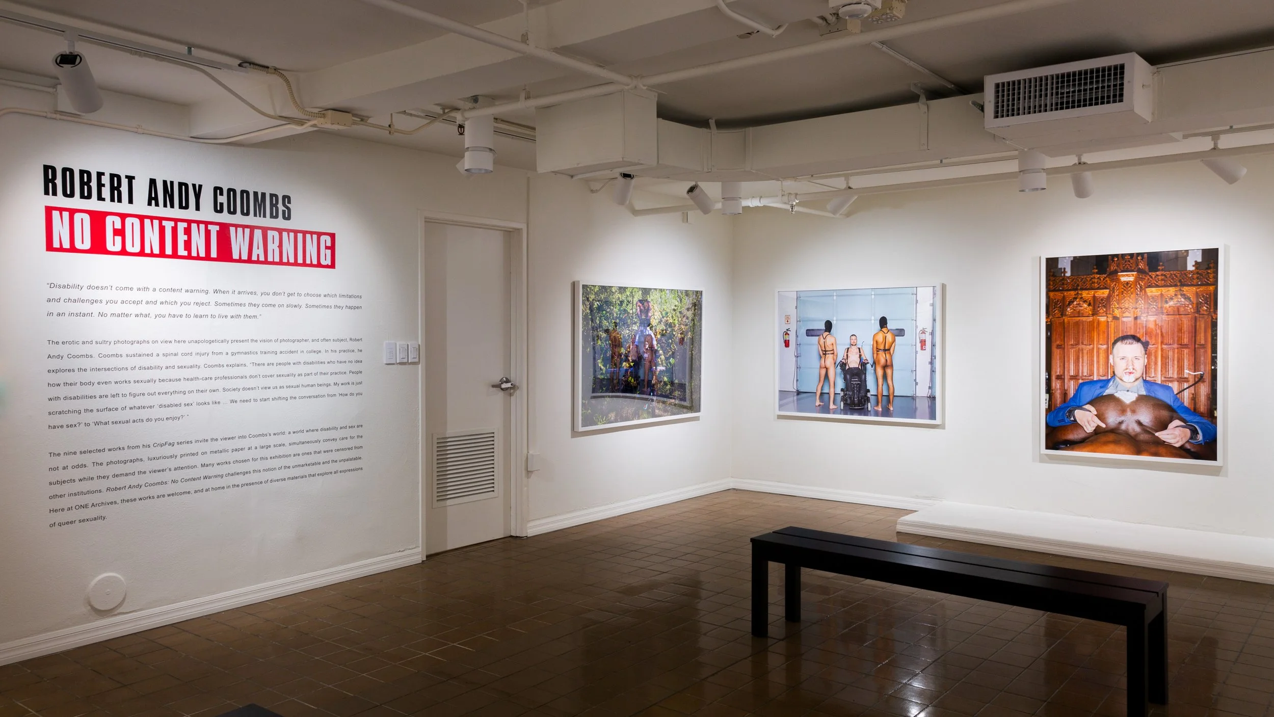 Gallery wall with photographs and a large text panel titled 'Robert Andy Coombs: No Content Warning,' featuring images of people in various settings and a descriptive paragraph.