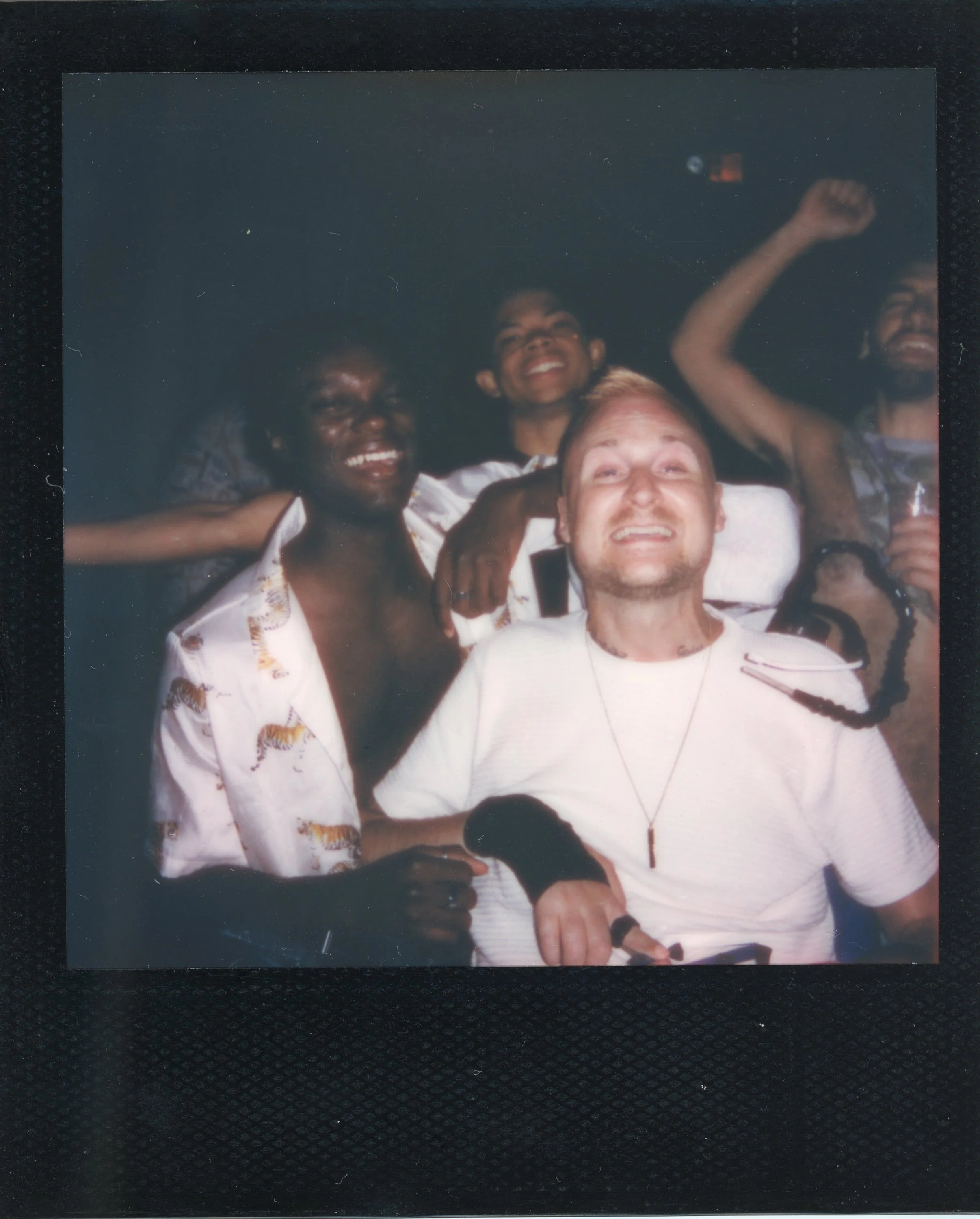 Group of five friends enjoying themselves in a dark setting, smiling and looking happy, with some raising their arms.