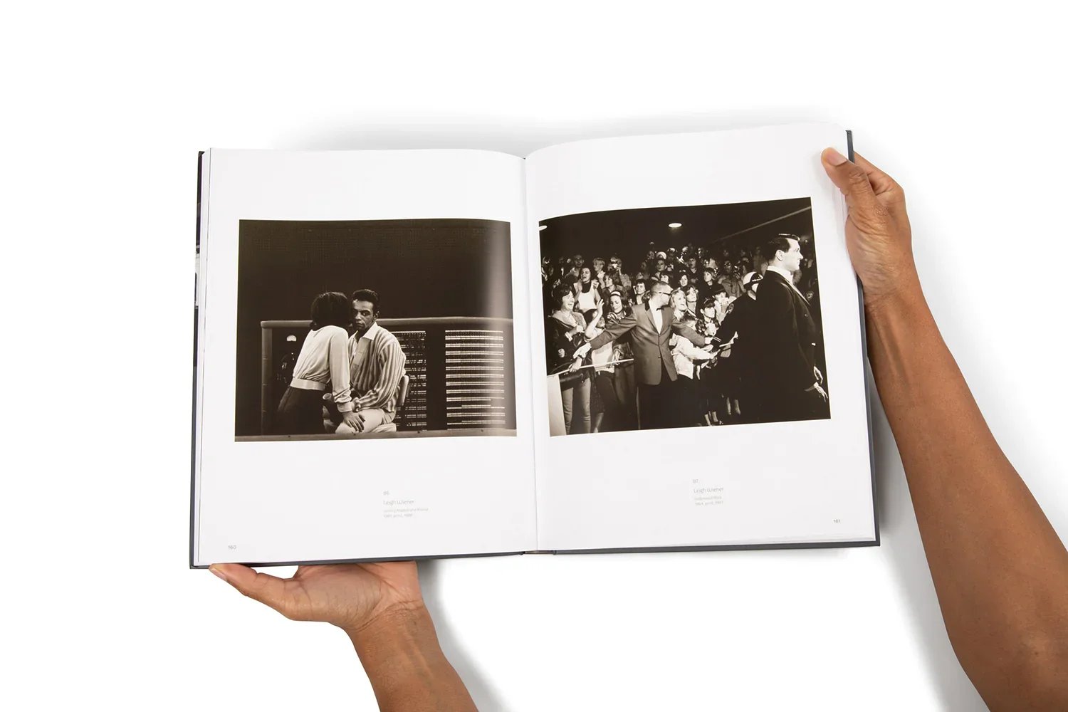Open photo book showing black and white images; left page has two people sitting and talking, right page shows a crowded scene with a person leading a group.