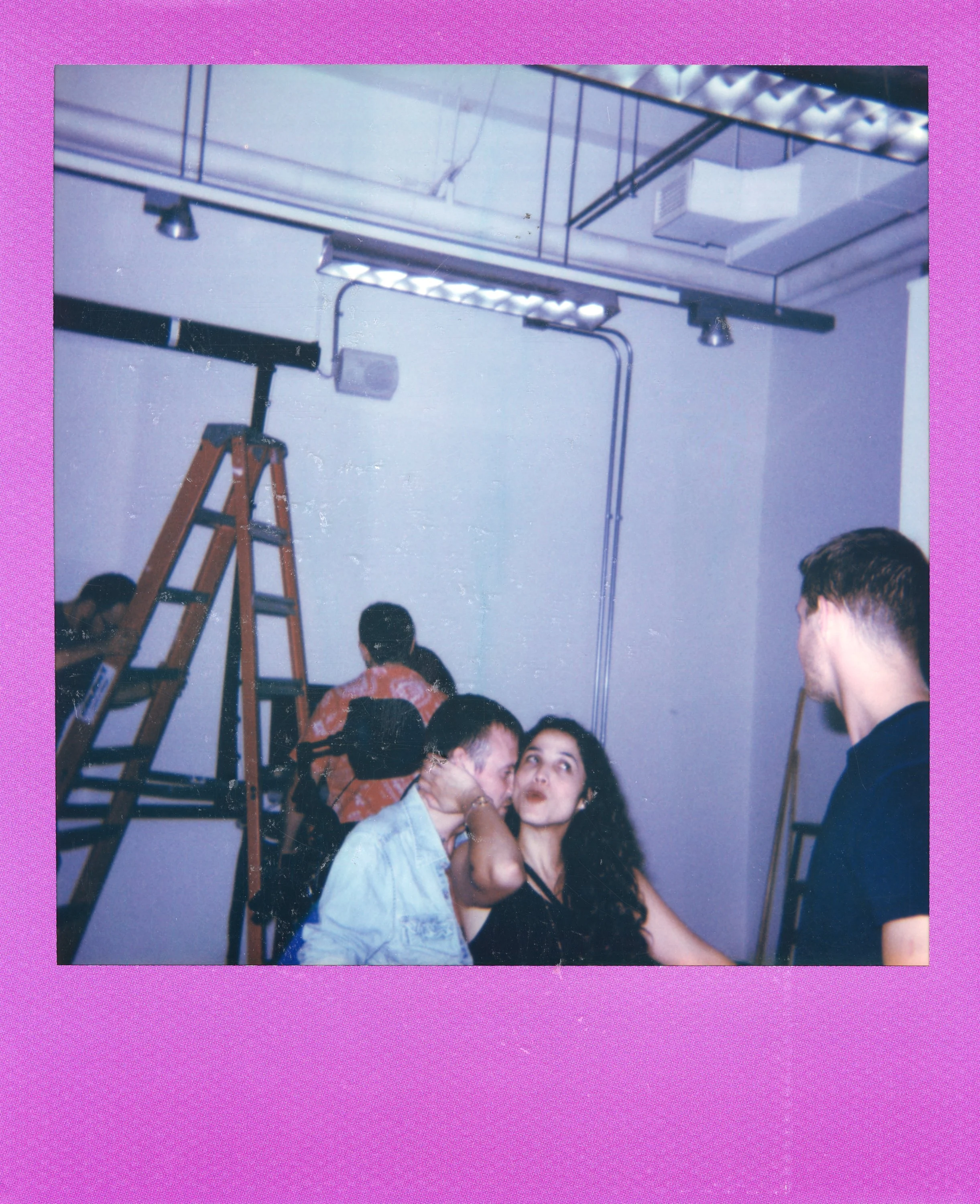 Group of people socializing in an indoor space with ladders and industrial ceiling lights.
