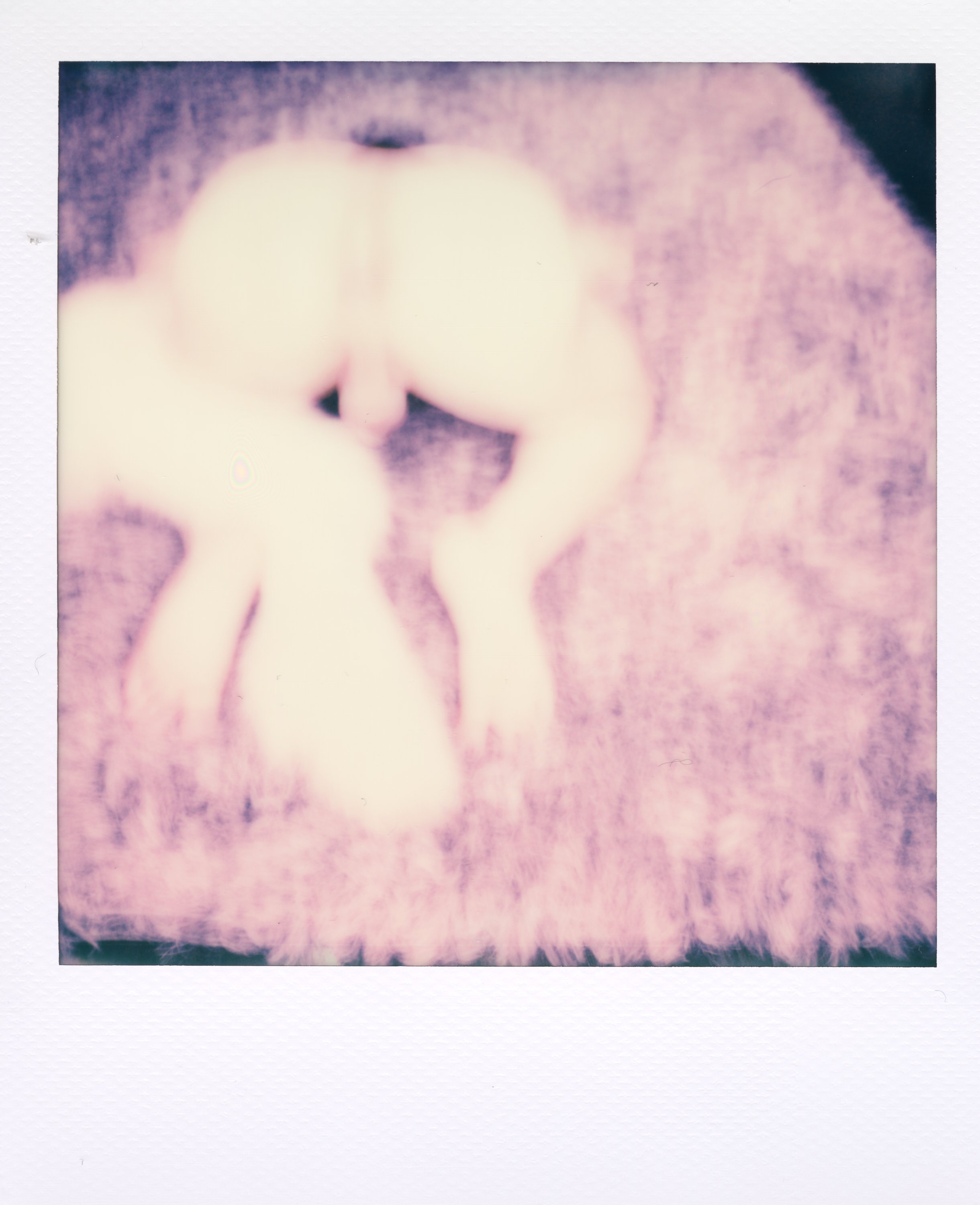 A person with light-colored hair sitting on a fuzzy pink carpet, viewed from behind and above, with their knees bent and their head slightly down.