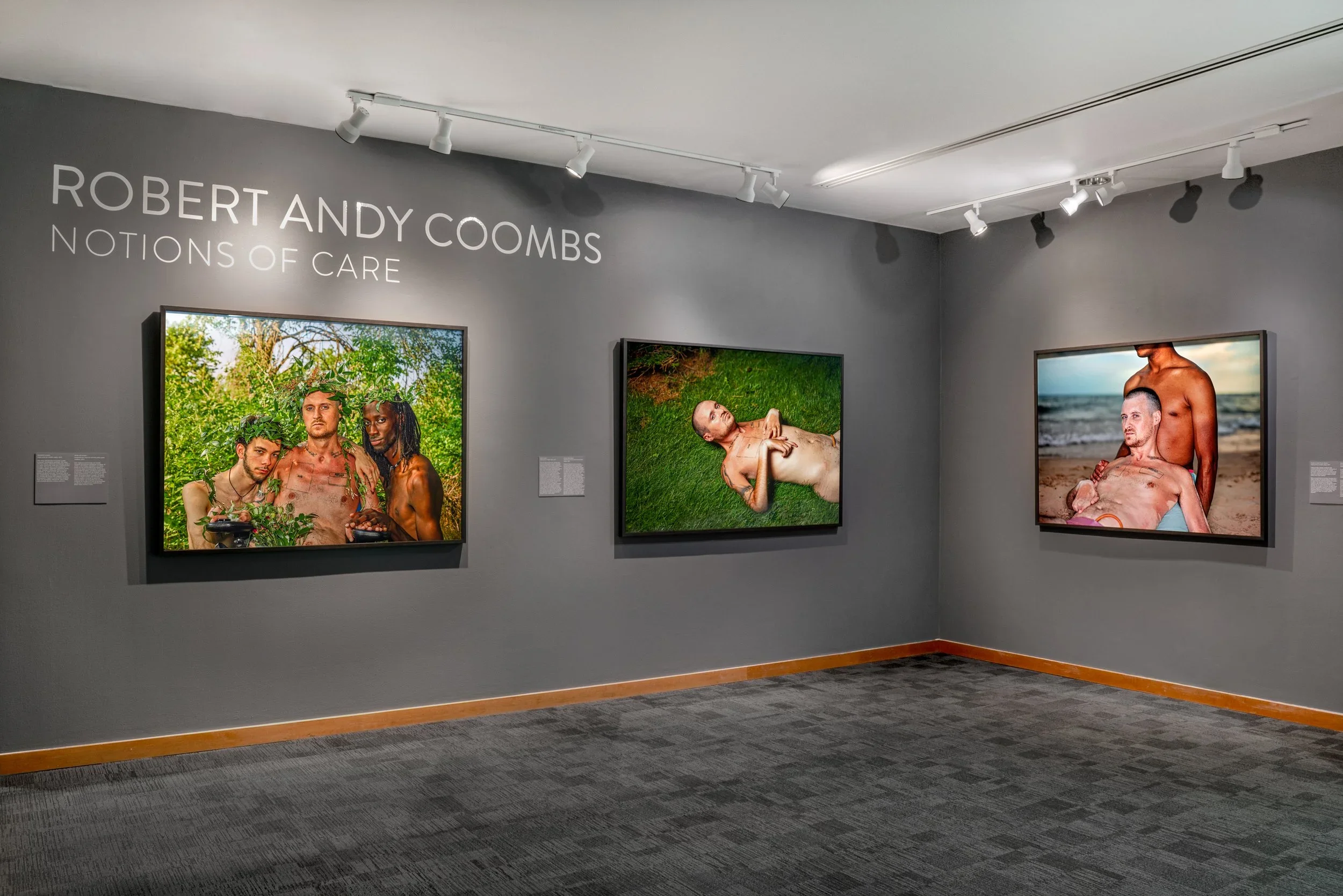 Gallery wall displaying three photographs by Robert Andy Coombs titled 'Notions of Care', featuring LGBTQ+ individuals in natural and outdoor settings.