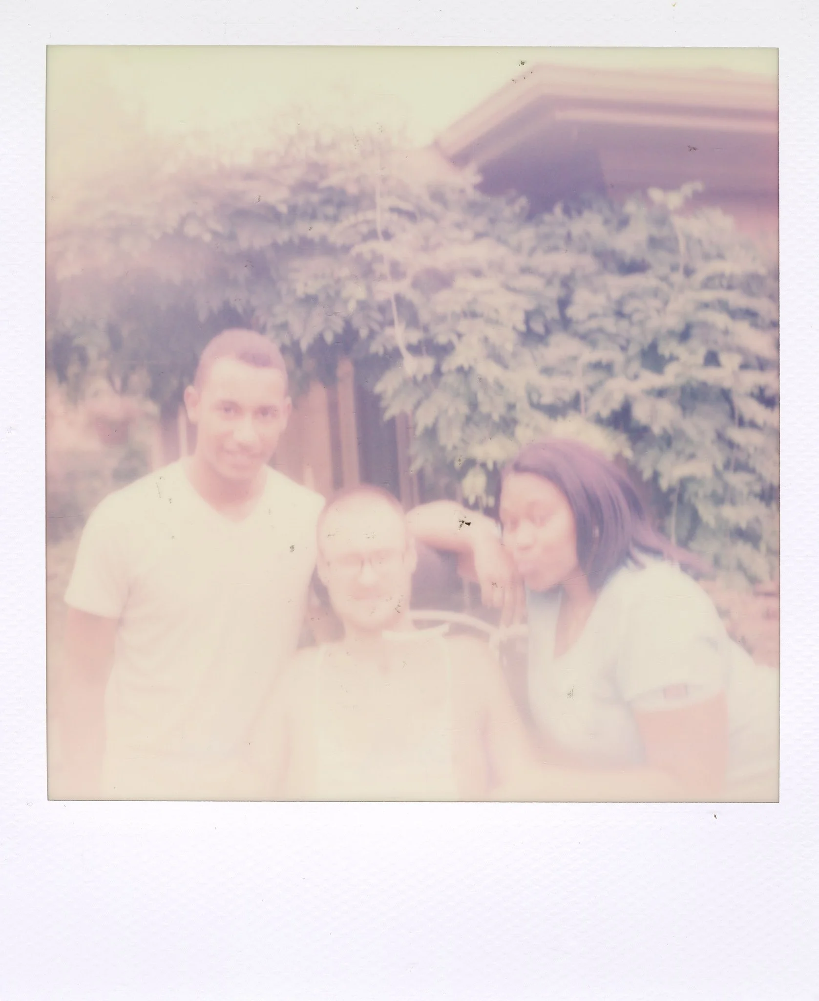 Three people standing outdoors, one man and two women, with greenery and a house in the background.