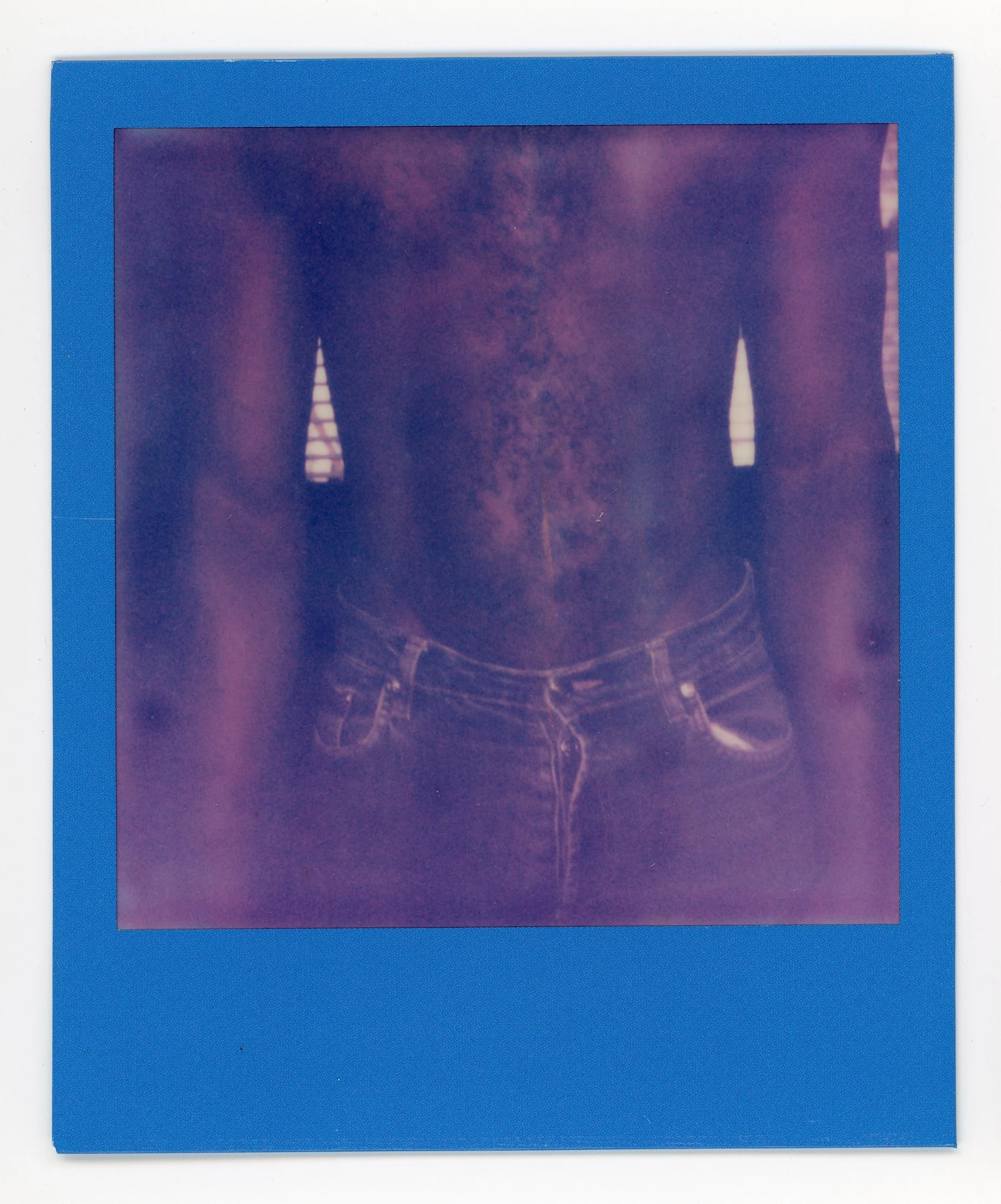 Polaroid photo showing the midsection of a person wearing a cropped top with vertical striped straps and denim shorts. The photo has a purple hue.