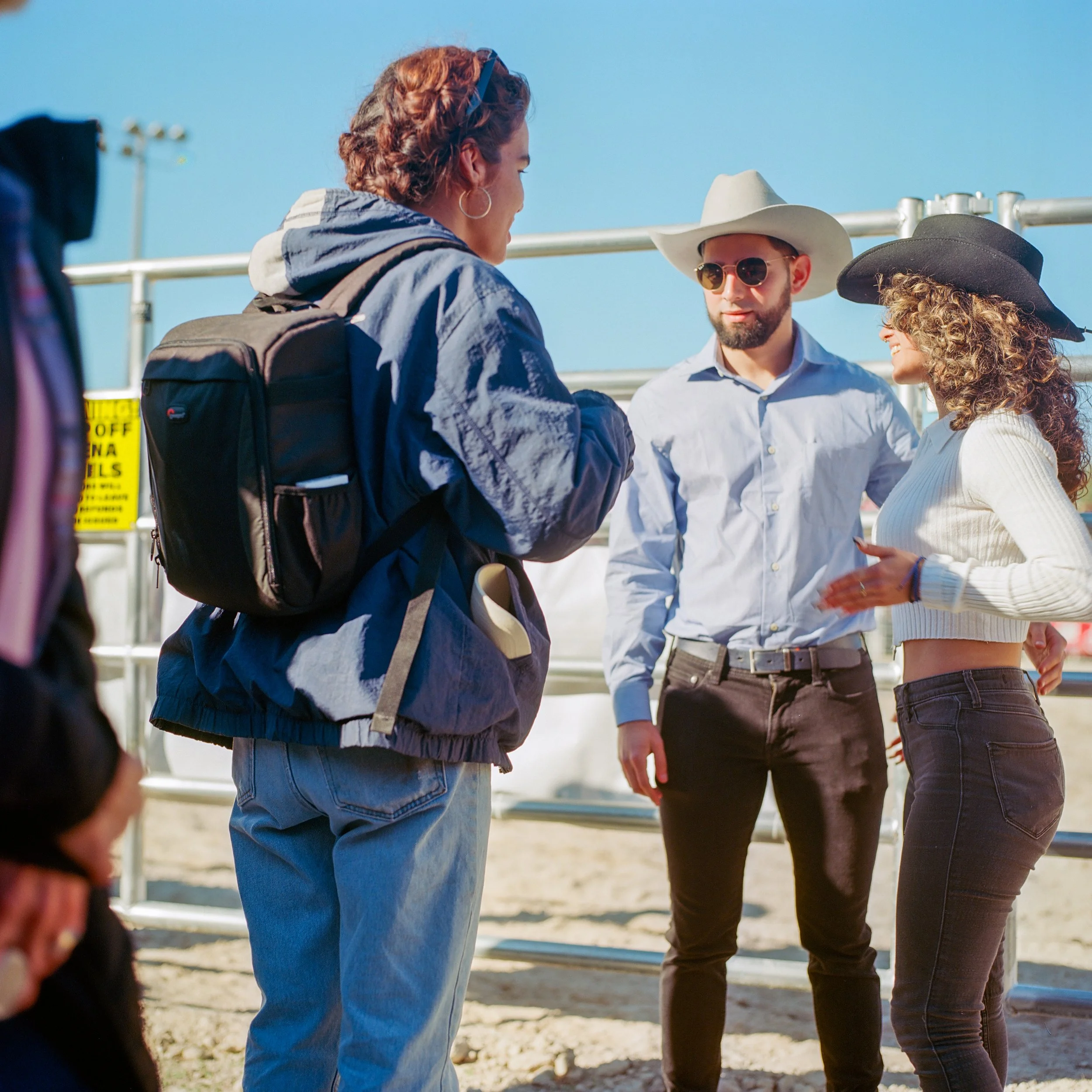 Three young adults, two women and one man, are outdoors, wearing cowboy hats and casual clothes, engaged in a conversation.