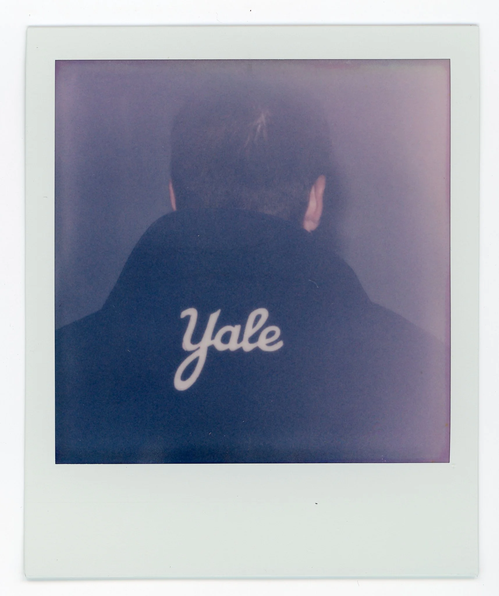 Back of a person wearing a black hoodie with 'Yale' written on it, photo taken from behind, within a white border frame.