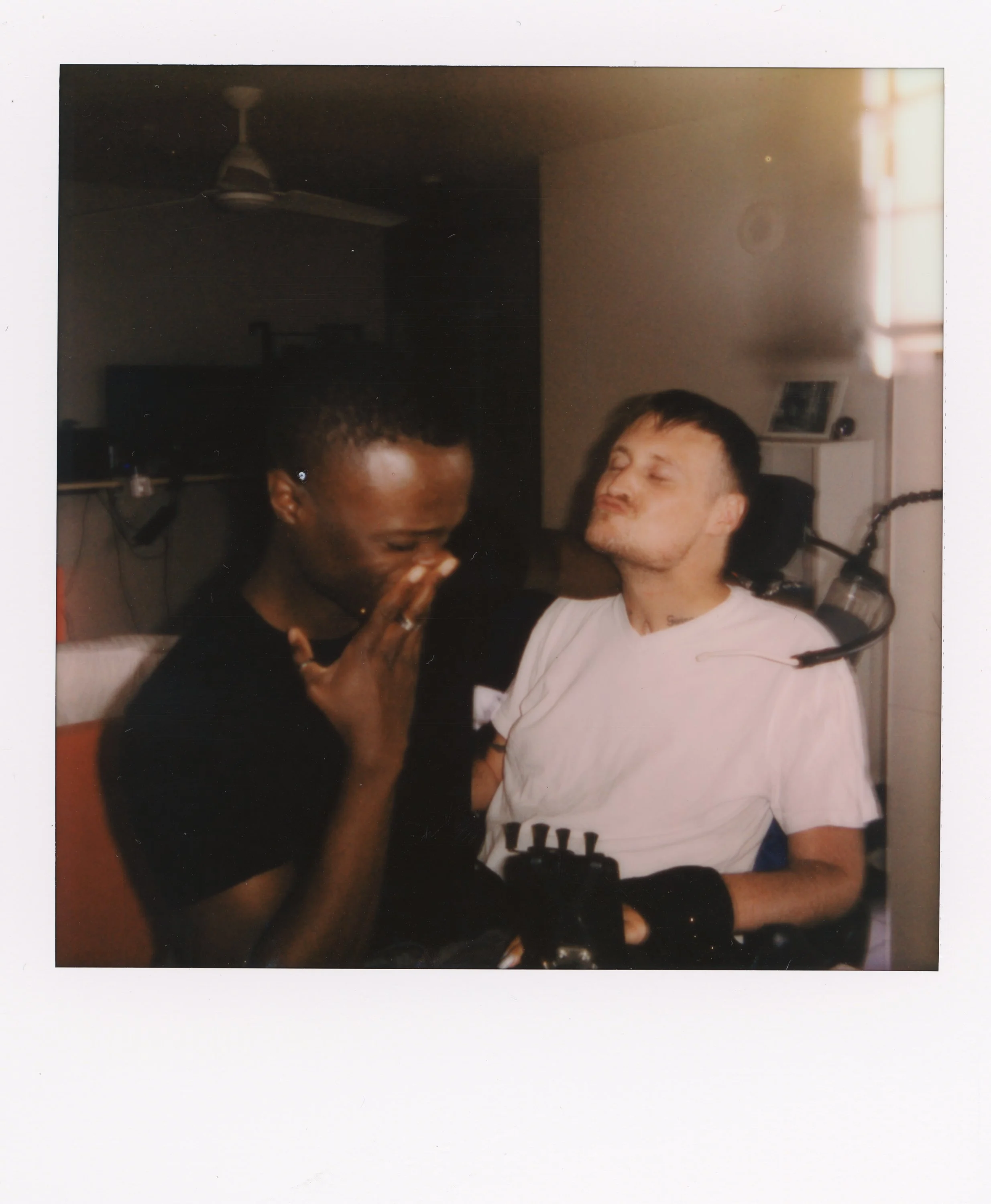 Two men, one Black and one White with a disability, sharing a moment of laughter together in a room with natural light.