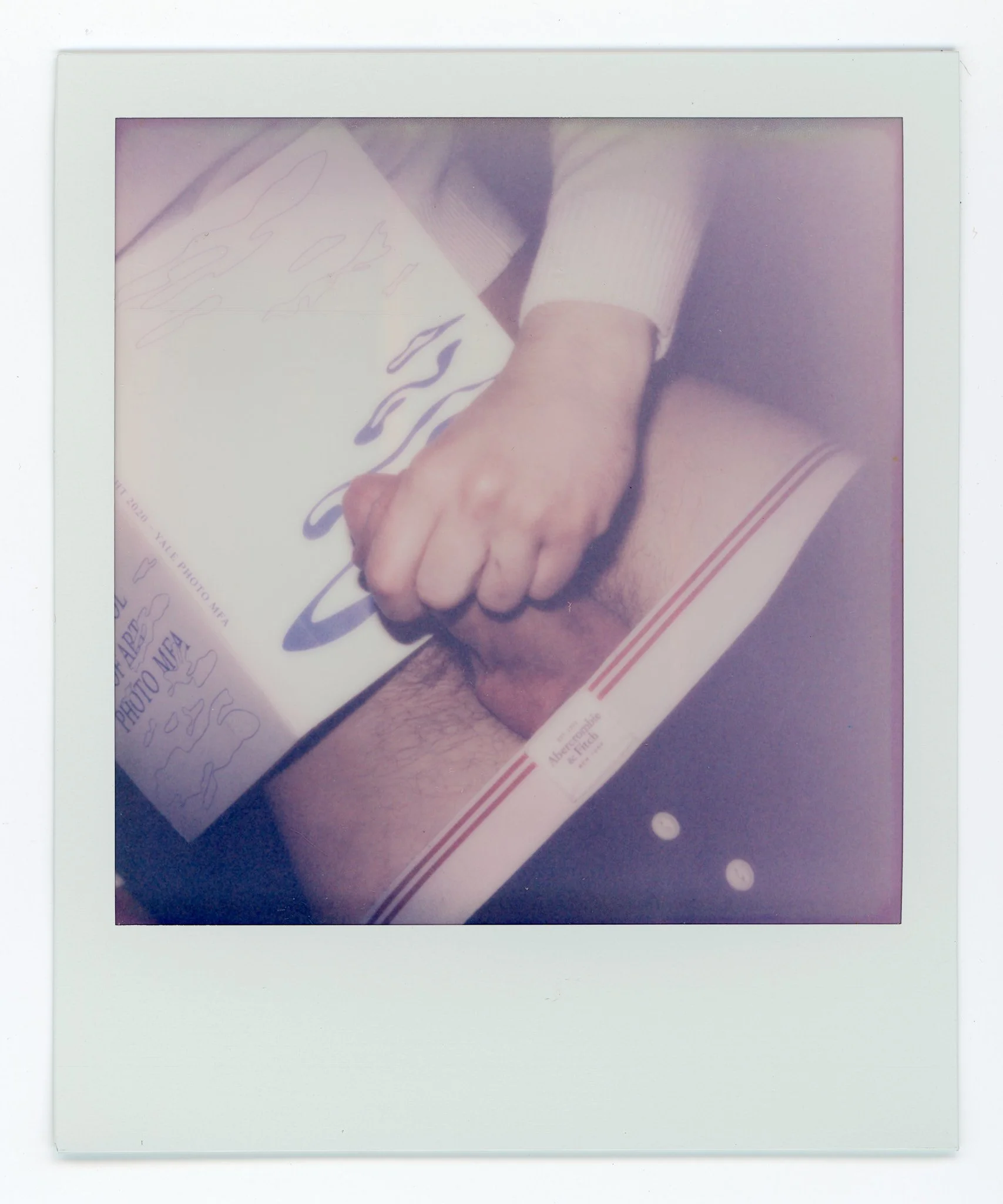 Close-up of a person's hand holding a signed photograph of a shirtless man with hairy chest, lying on a bed, with part of the person's arm and clothing visible.