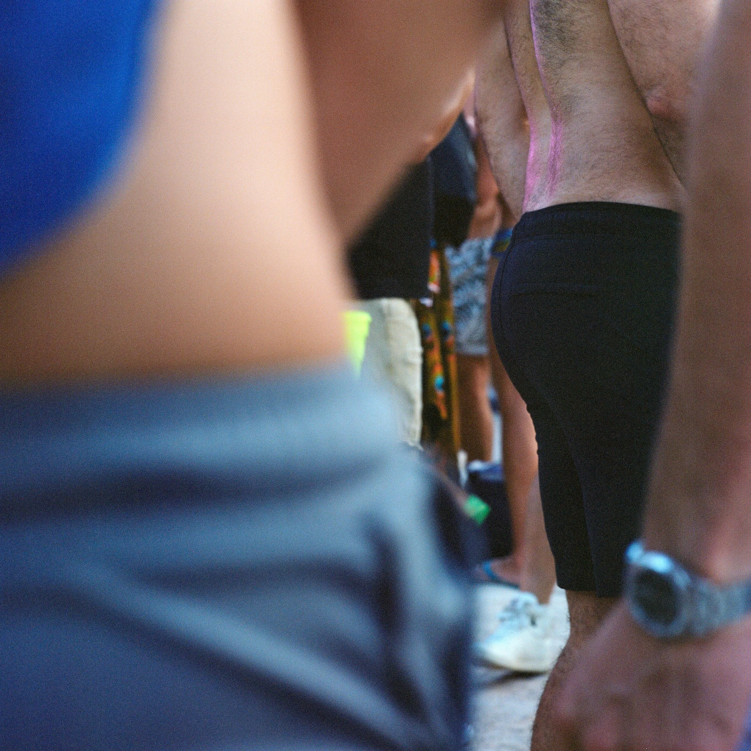 Close-up of bare torsos and legs of people participating in a race or event, with some wearing athletic gear and watches.