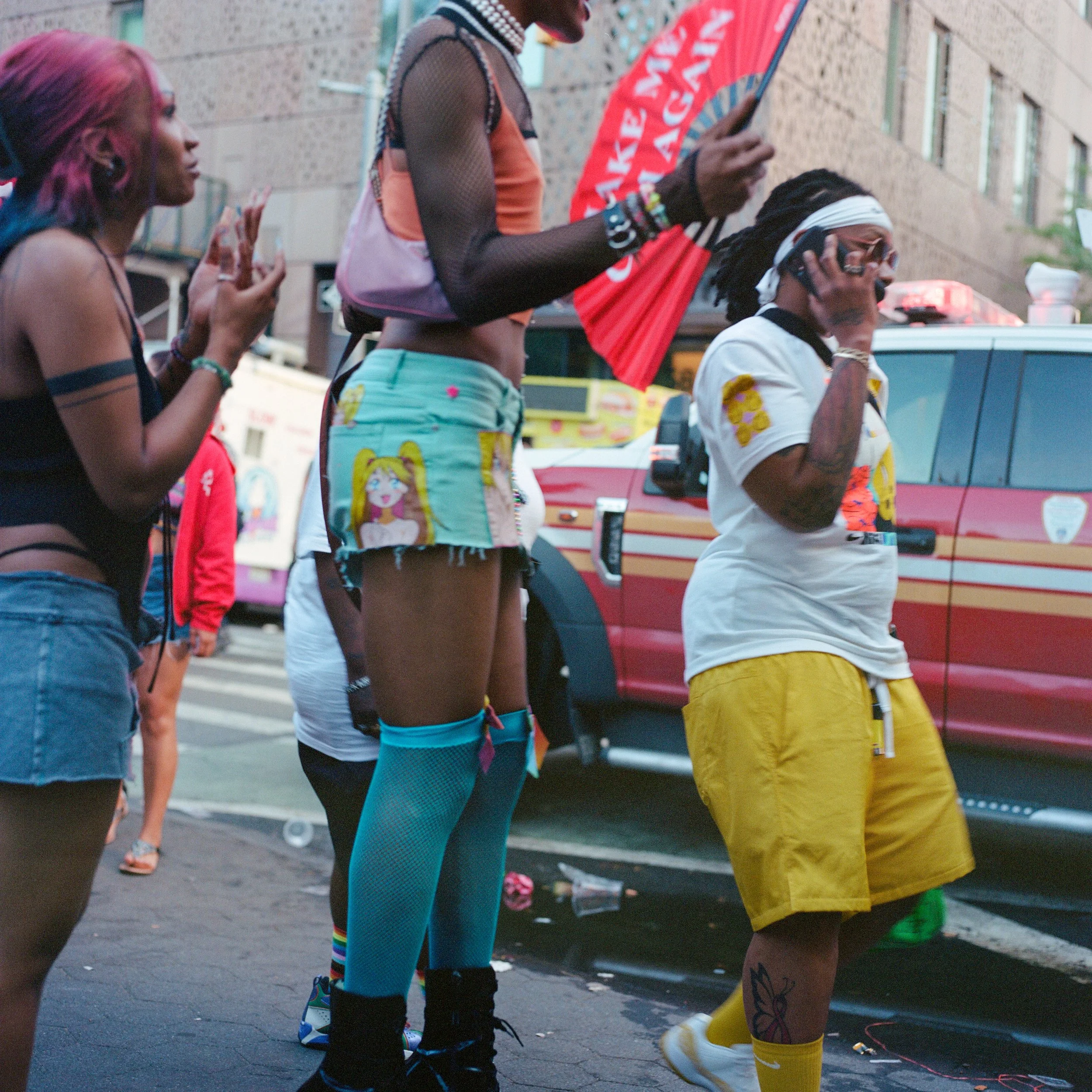 People standing on city street, one person holding a phone, others clapping, with a fire truck in the background.