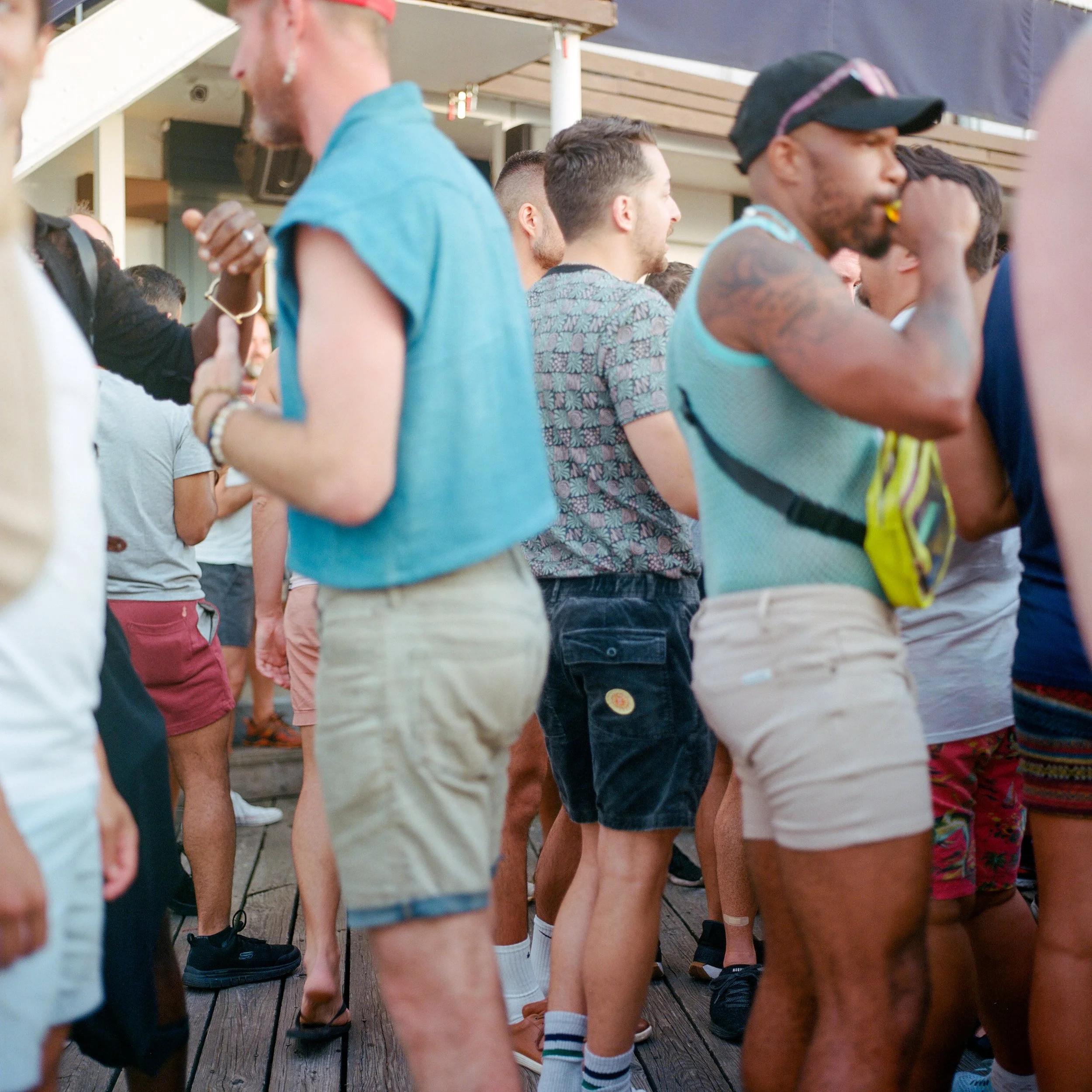 Group of people standing on a wooden deck, dressed in summer clothing, engaging in conversation.