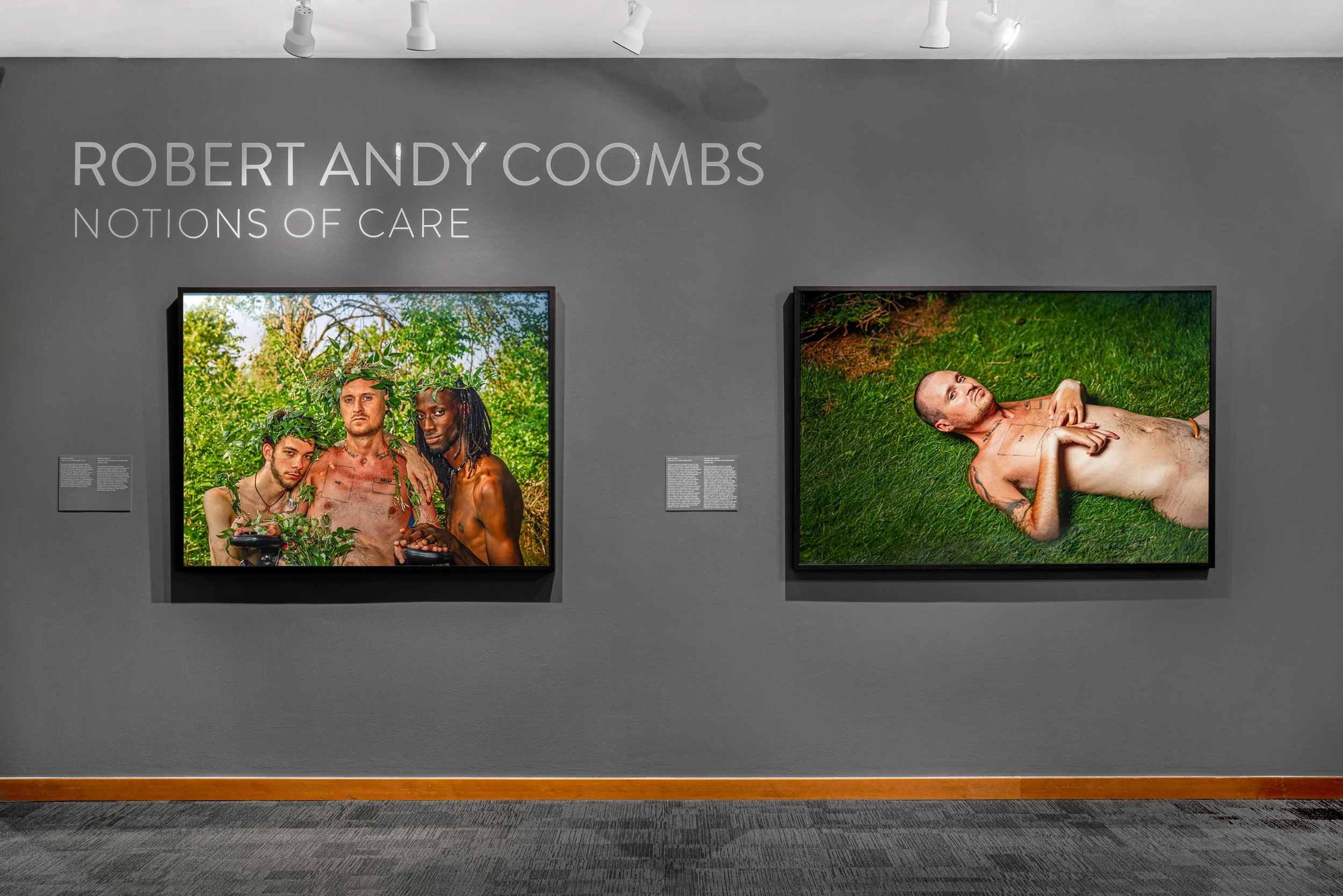 Two photographs from the exhibition 'Notions of Care' by Robert Andy Coombs. The left photo shows three men with various skin tones, shirtless, with leafy headpieces, standing outdoors among green trees. The right photo depicts a shirtless, tattooed