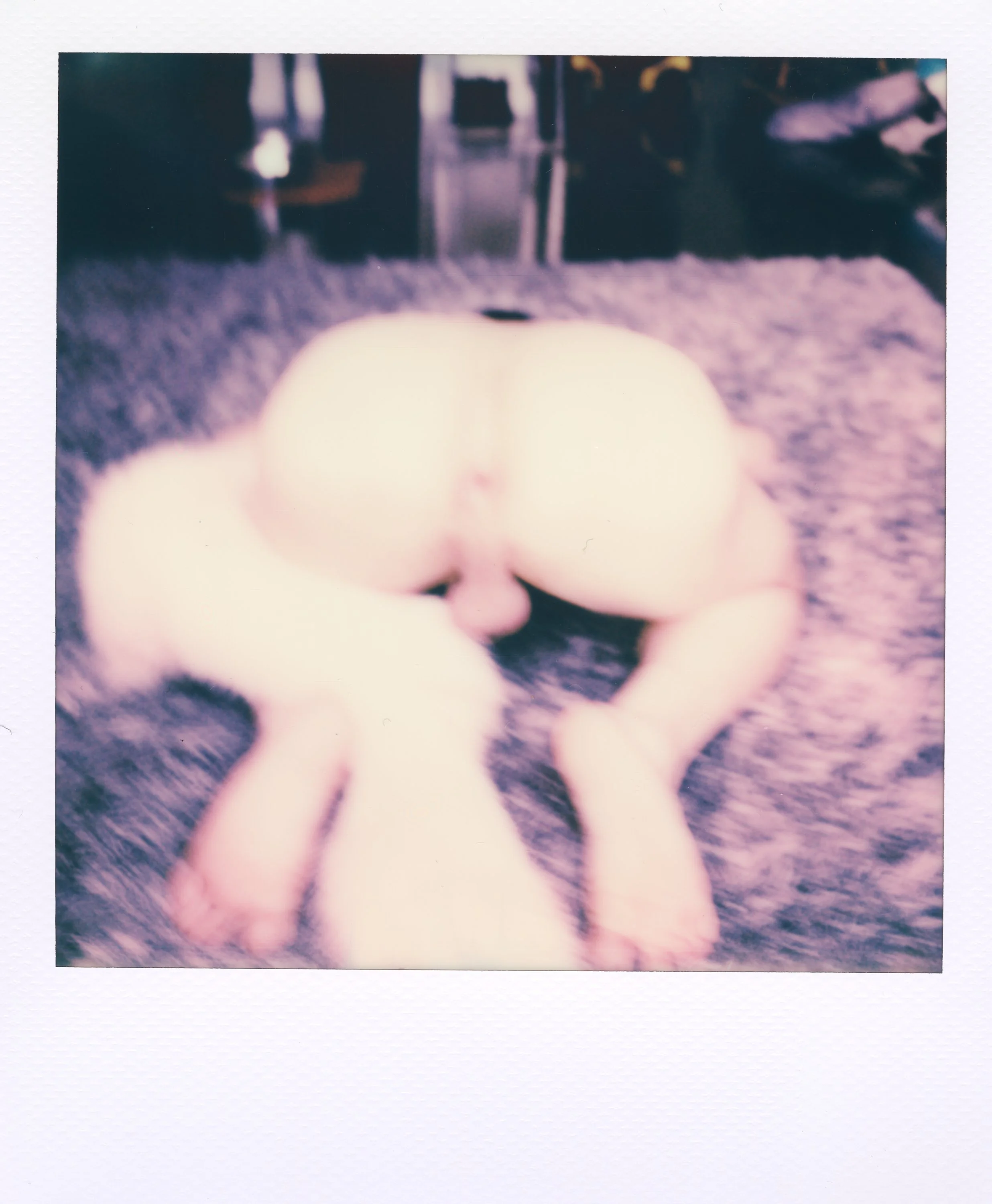 A blurred Polaroid photo of two naked people lying face-to-face on a furry surface, with a man positioned behind a woman, facing downward.
