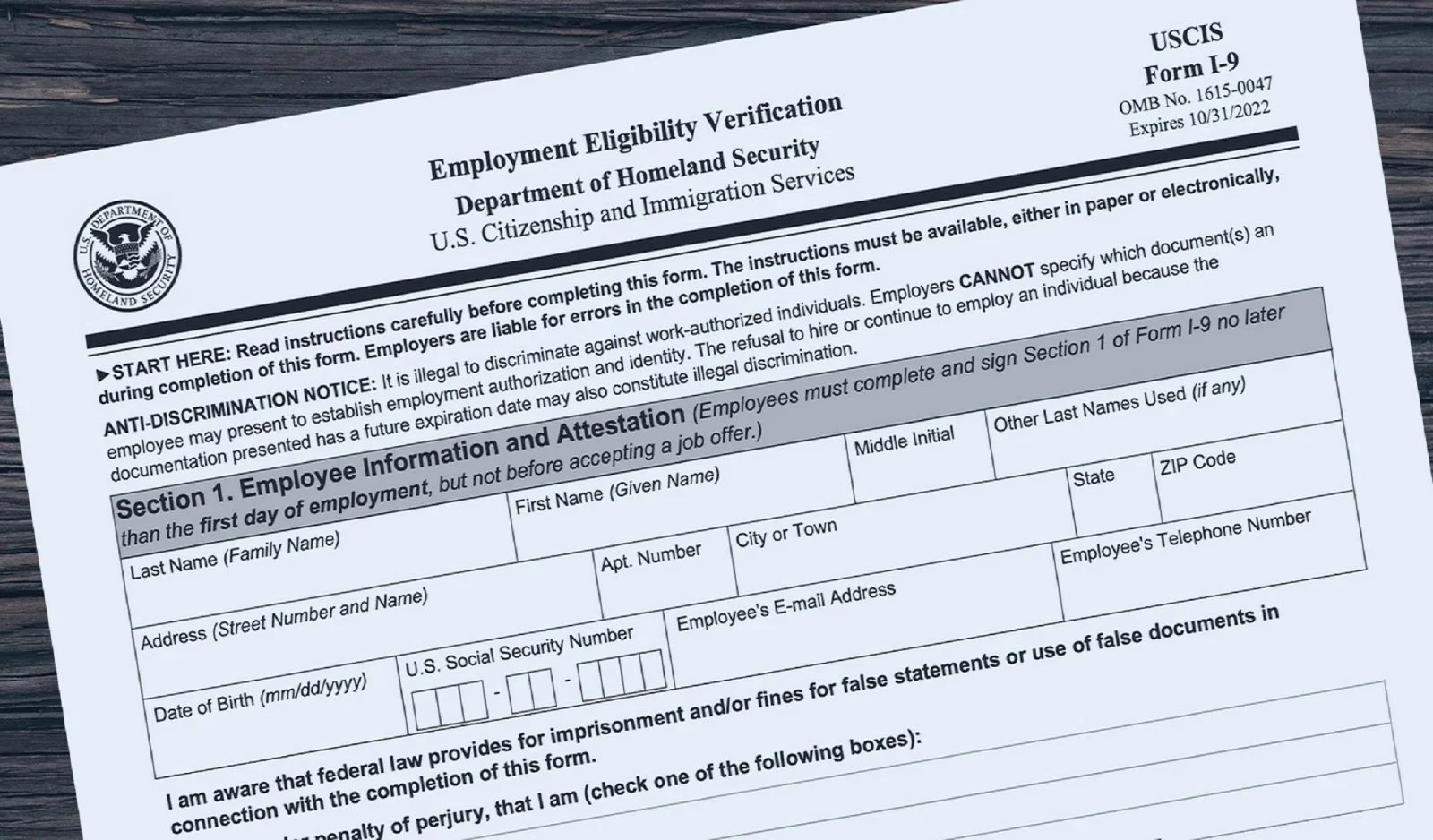 A U.S. Department of Homeland Security employment verification form (Form I-9) titled 'Employment Eligibility Verification' on a wooden surface.