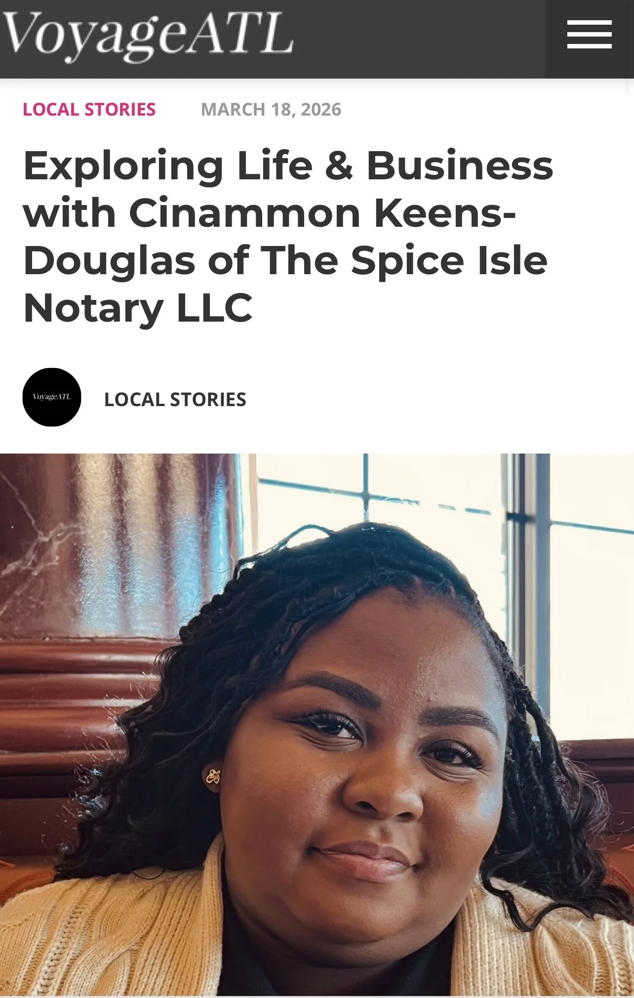 A woman with dark, curly hair and a light brown sweater, smiling softly in front of a window with light streaming through.