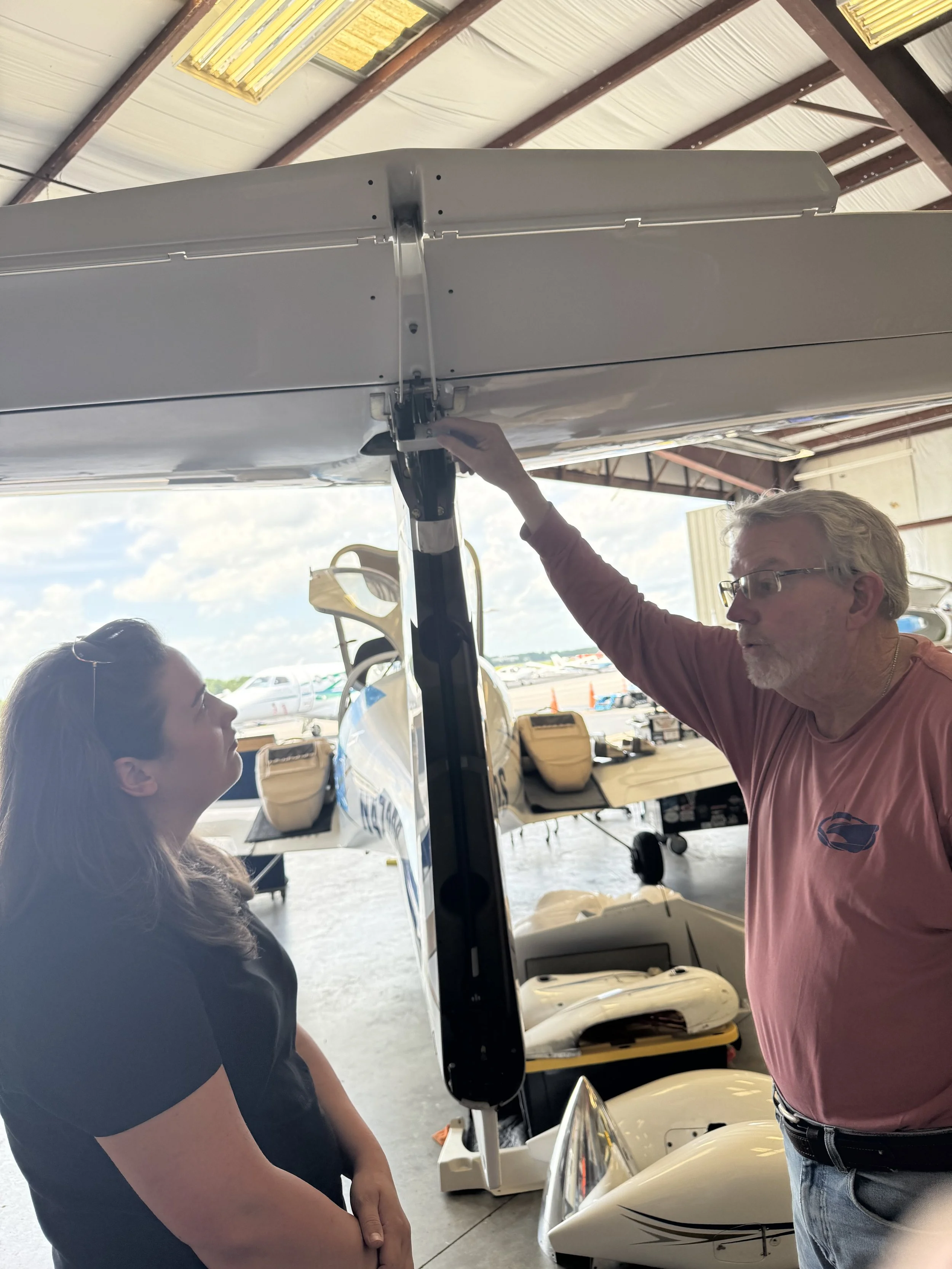 Female flight instructor standing inside a hangar near aircraft discussing flight training and rudder control. 