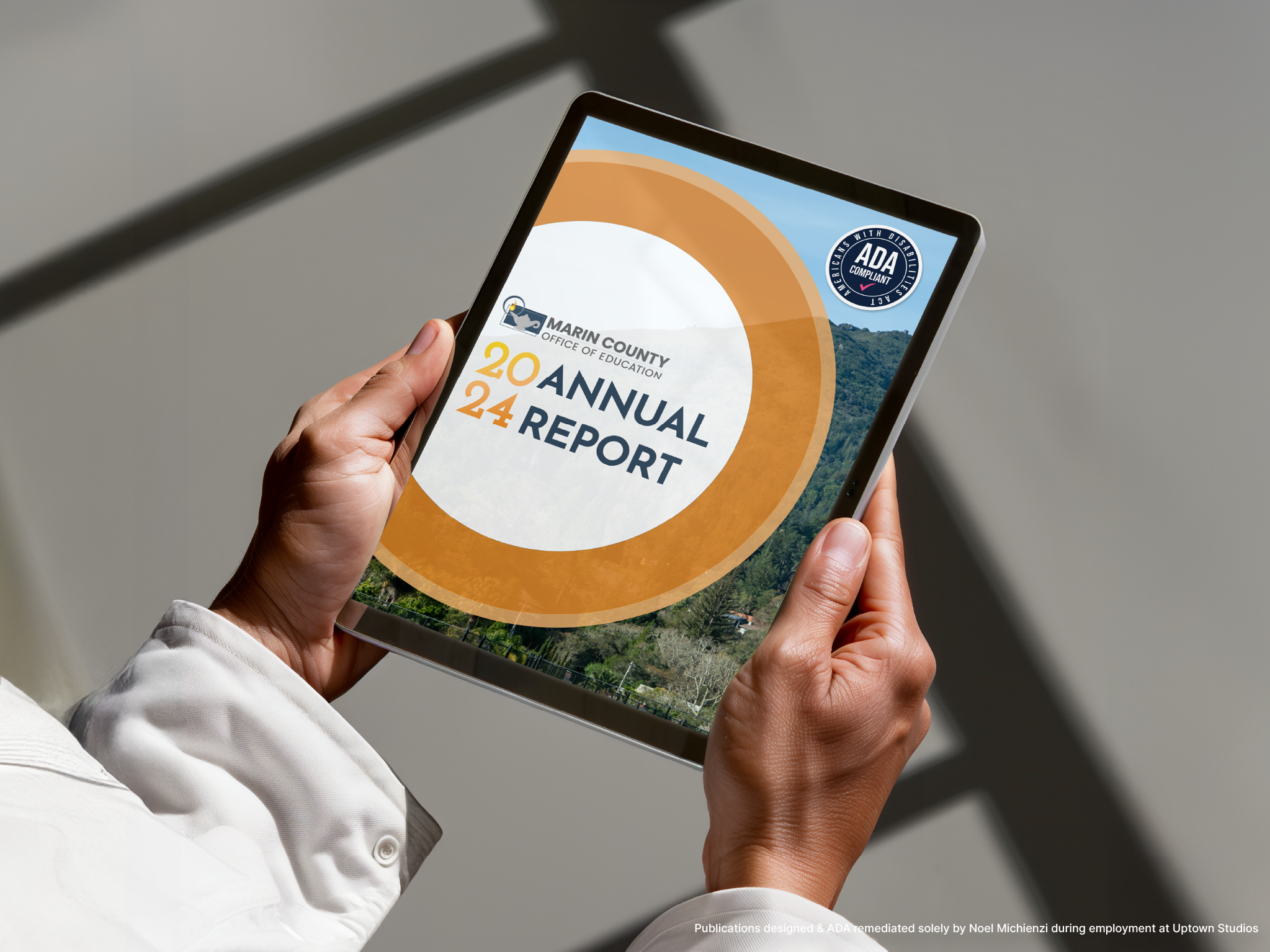 A person holding a tablet displaying the cover of the Marin County Office of Education's 2020-2024 Annual Report, which includes a logo, a circular design, and a scenic background.
