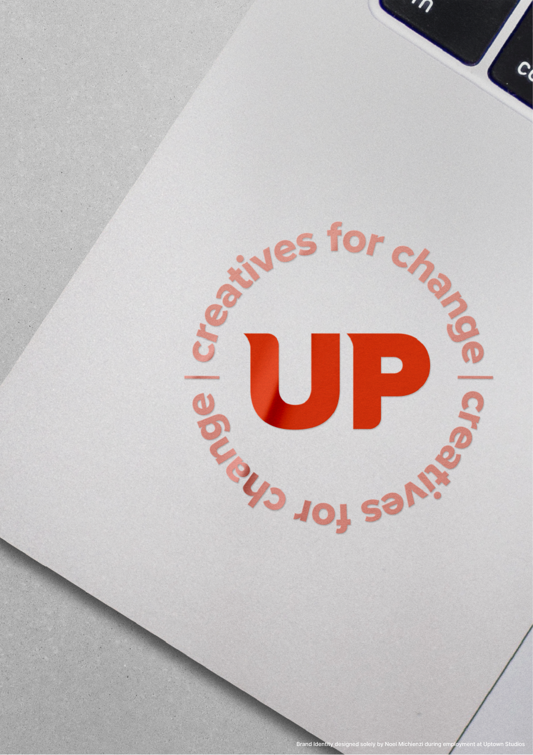 A circular logo that reads 'creatives for change' around the perimeter with large red letters 'UP' in the center, on a light-colored surface with a small part of a keyboard in the top right corner.