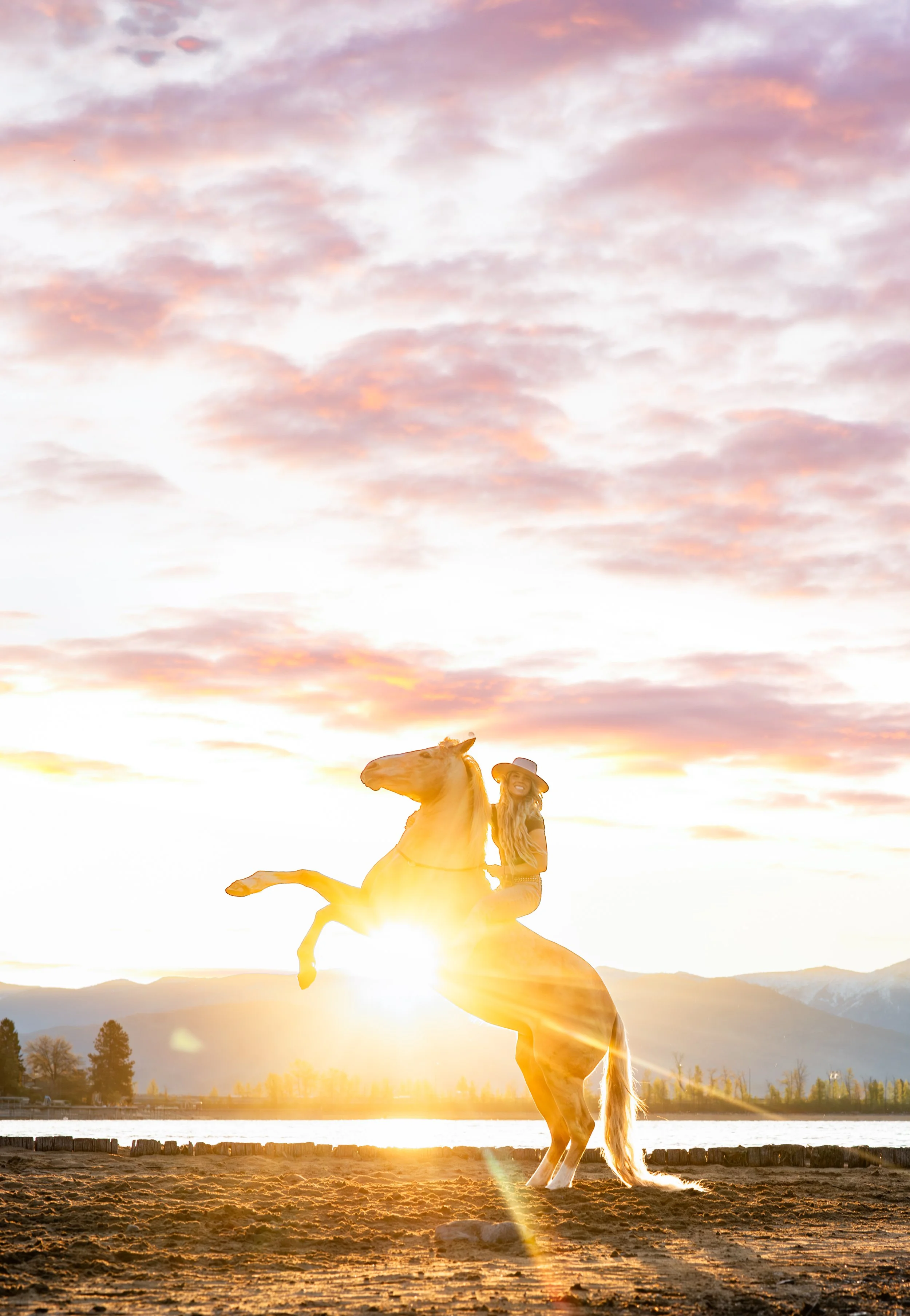 Wild Hearts Equestrian Connections riding a rearing horse during sunset with mountains and Lake Pend Oreille in the background.
