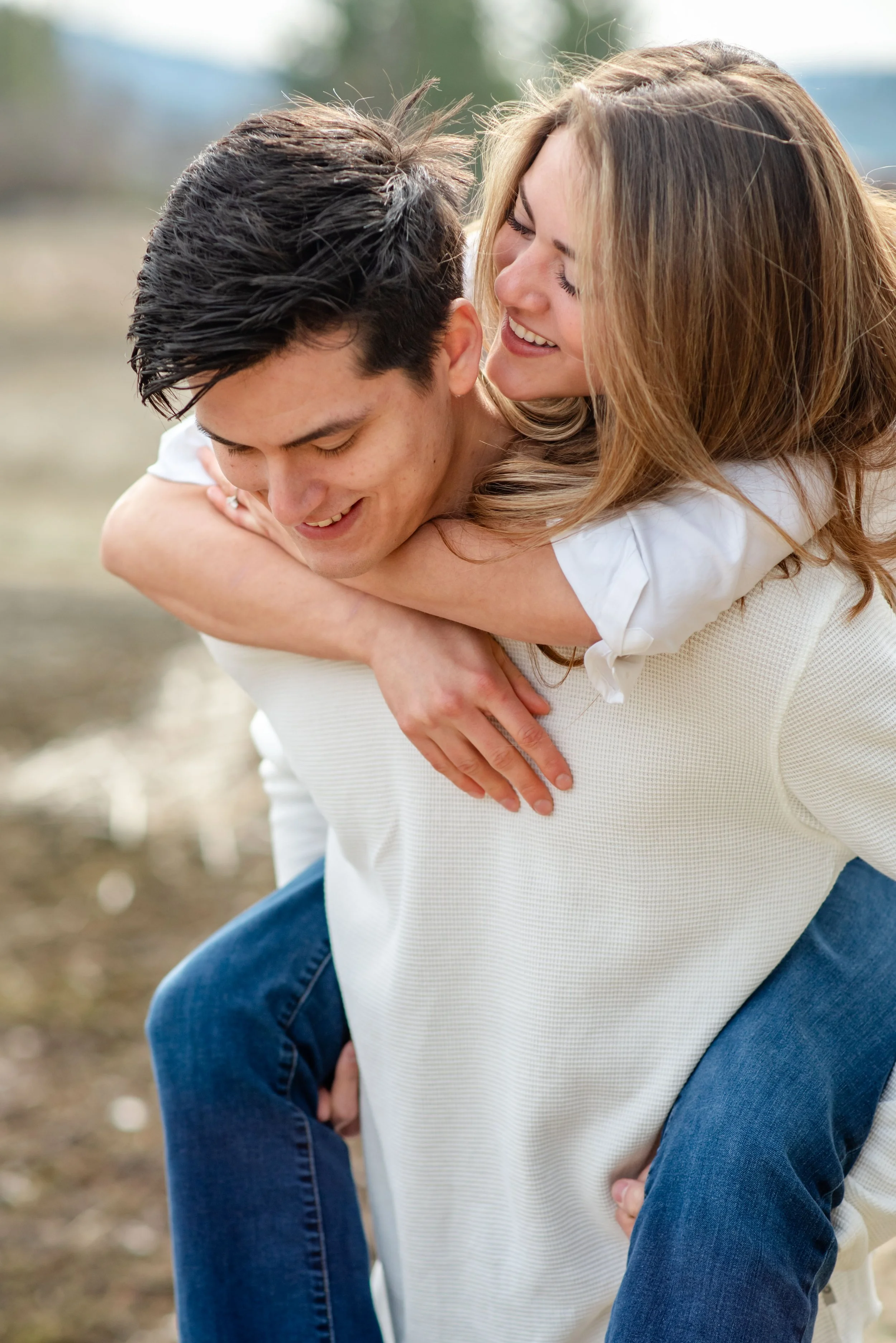 A woman giving a piggyback ride to a man outdoors, both smiling and enjoying each other's company.
