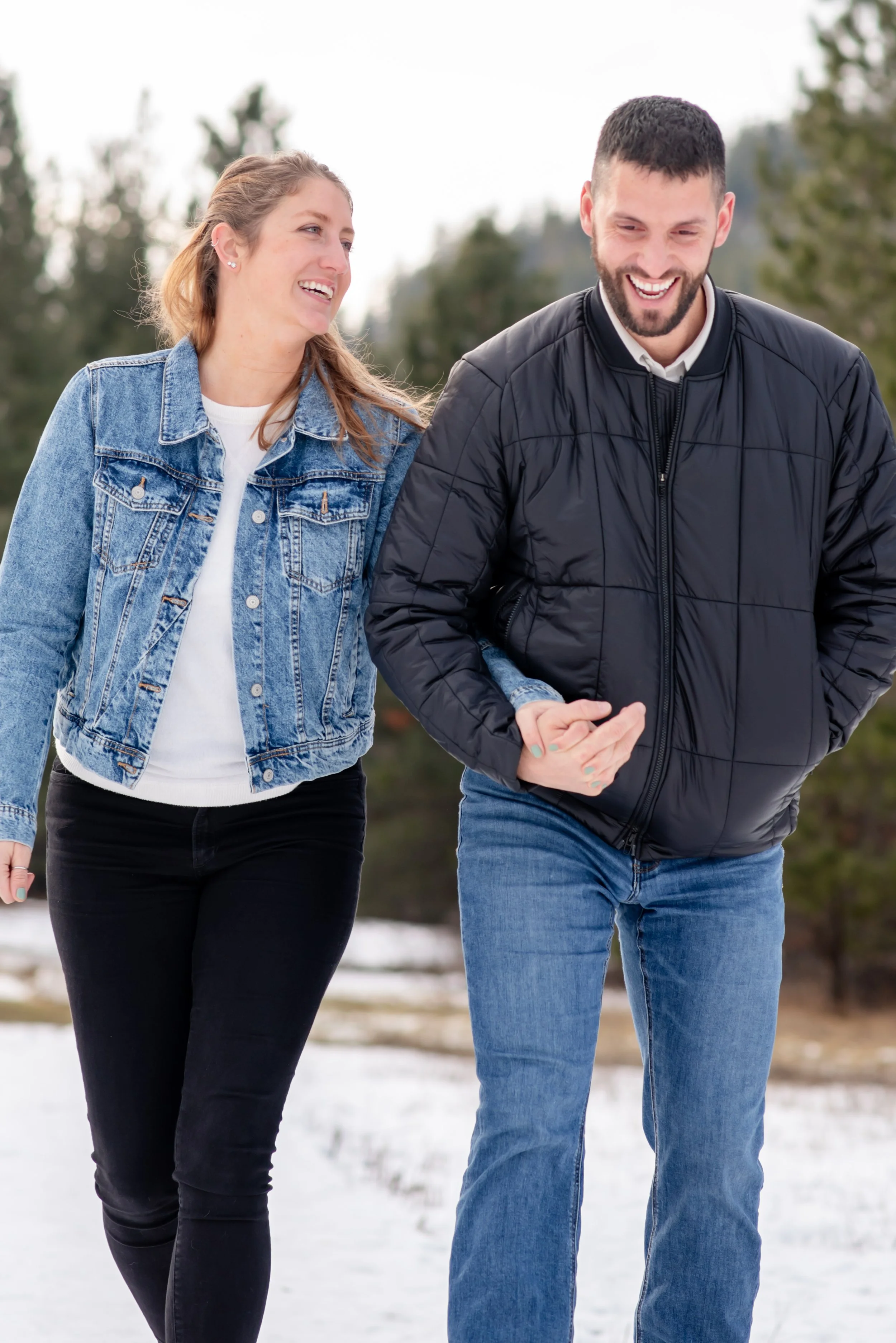 A smiling man and woman walking outdoors in a snowy landscape, holding hands.