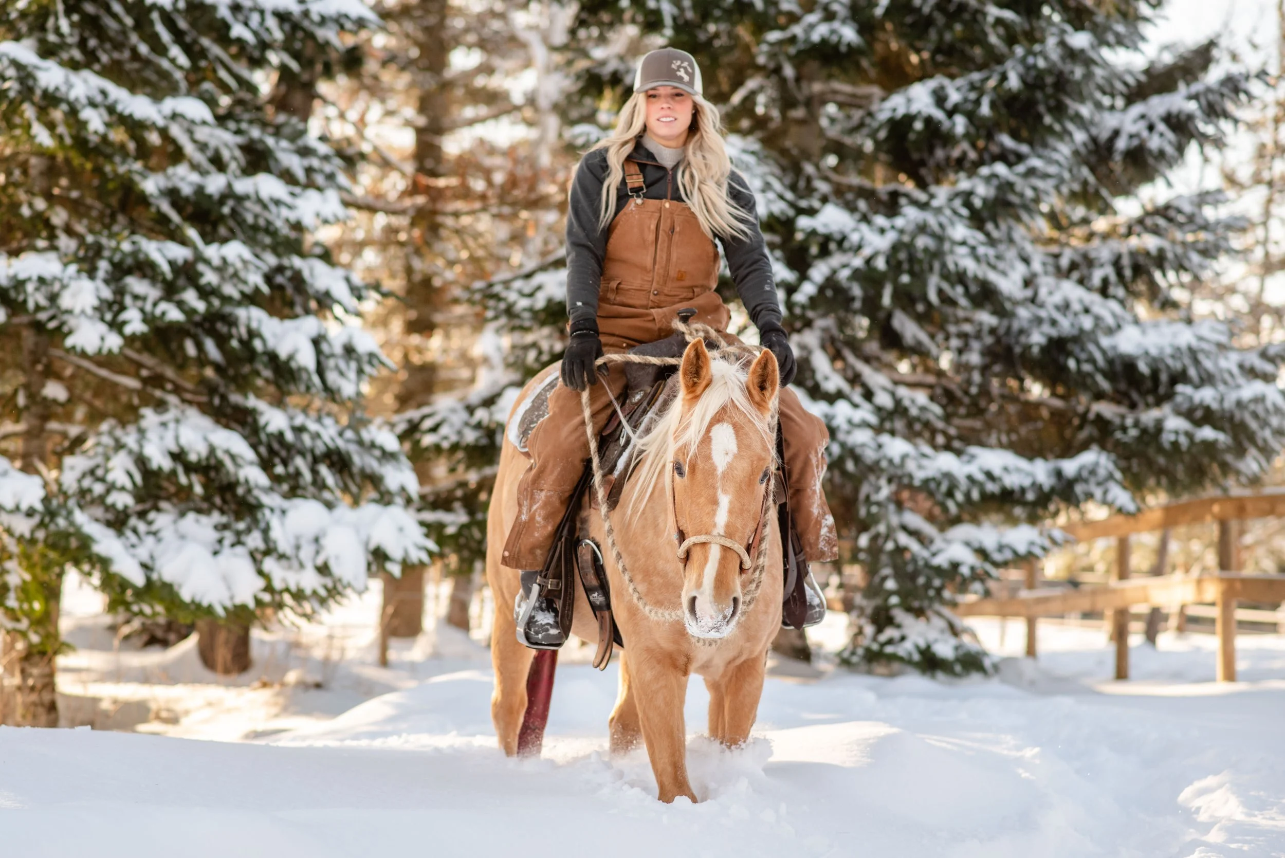 A woman riding a horse through snow in a wooded area with snow-covered trees.