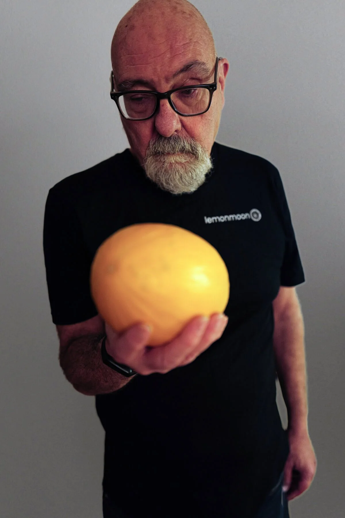 Paul with glasses, and a beard, holding a large yellow melon in his hand.