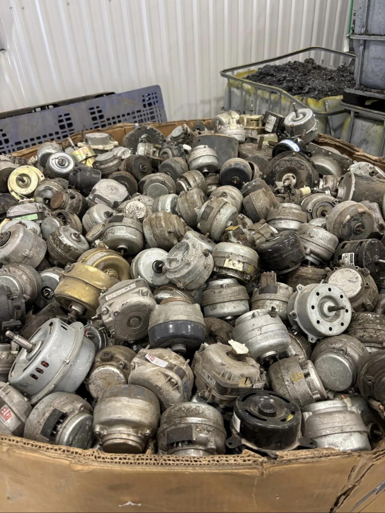 Box filled with numerous used or discarded motor alternators or starters stacked on top of each other.