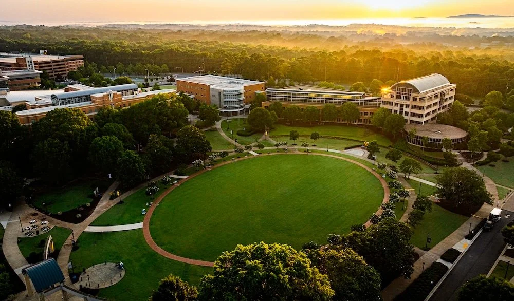 An aerial view of a university campus during sunset with buildings, green lawns, walking paths, and trees.