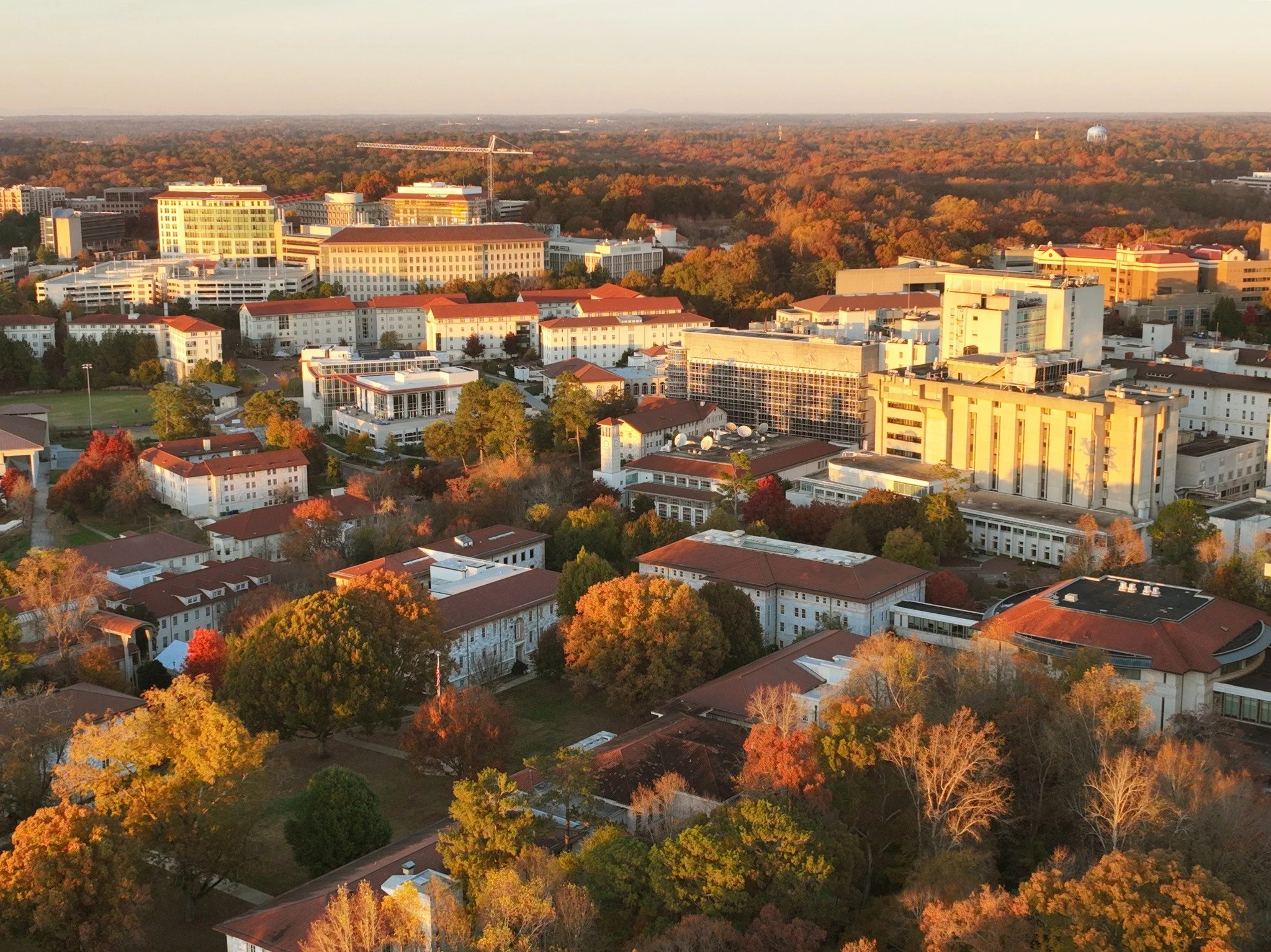 Aerial view of a emory university during autumn with colorful fall foliage, modern buildings, and a clear sky at sunset.