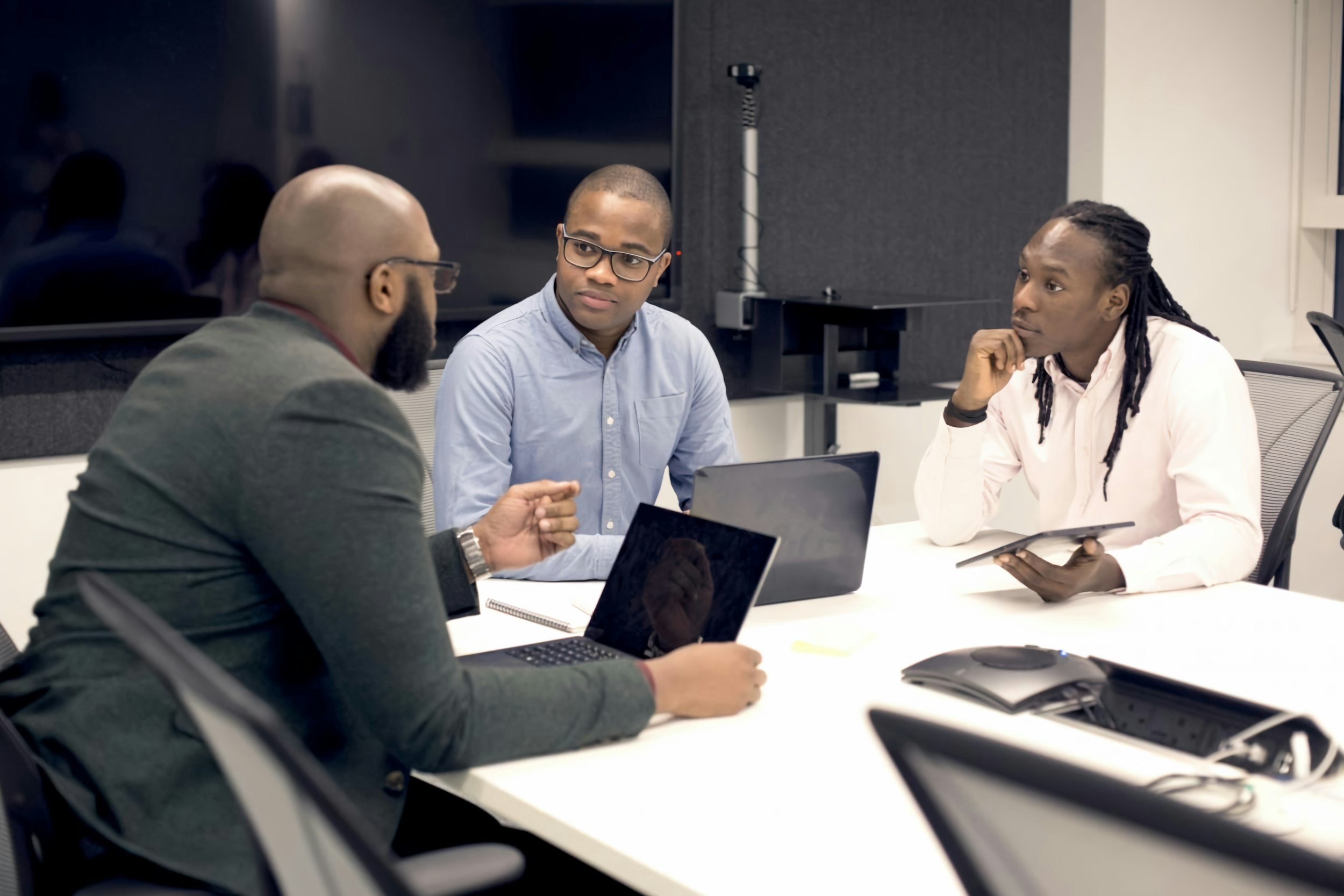Three men in a business meeting discussing around a laptop in a conference room.