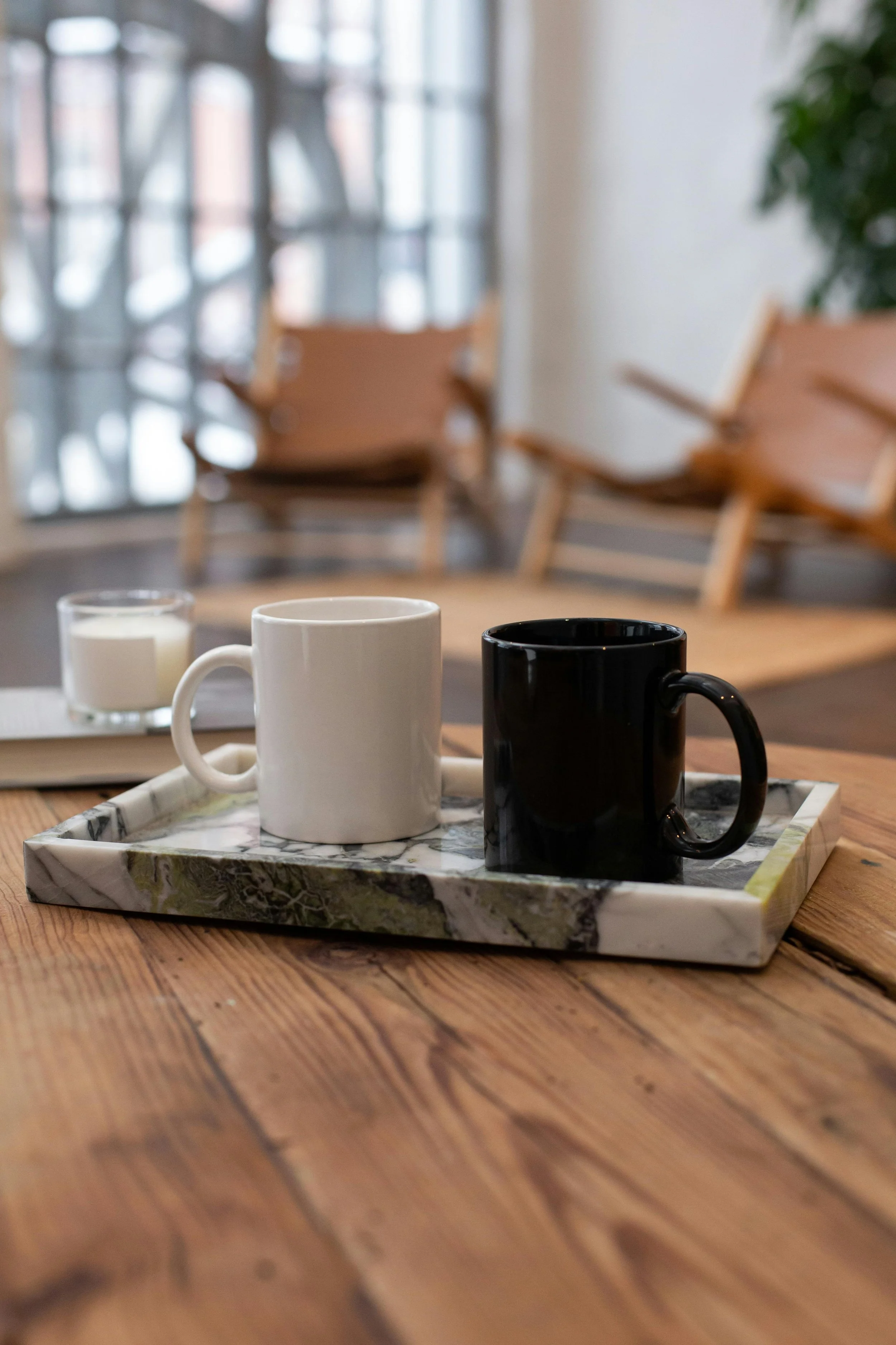 Two cups, one white and one black, placed on a marble tray on a wooden table in a cozy cafe.