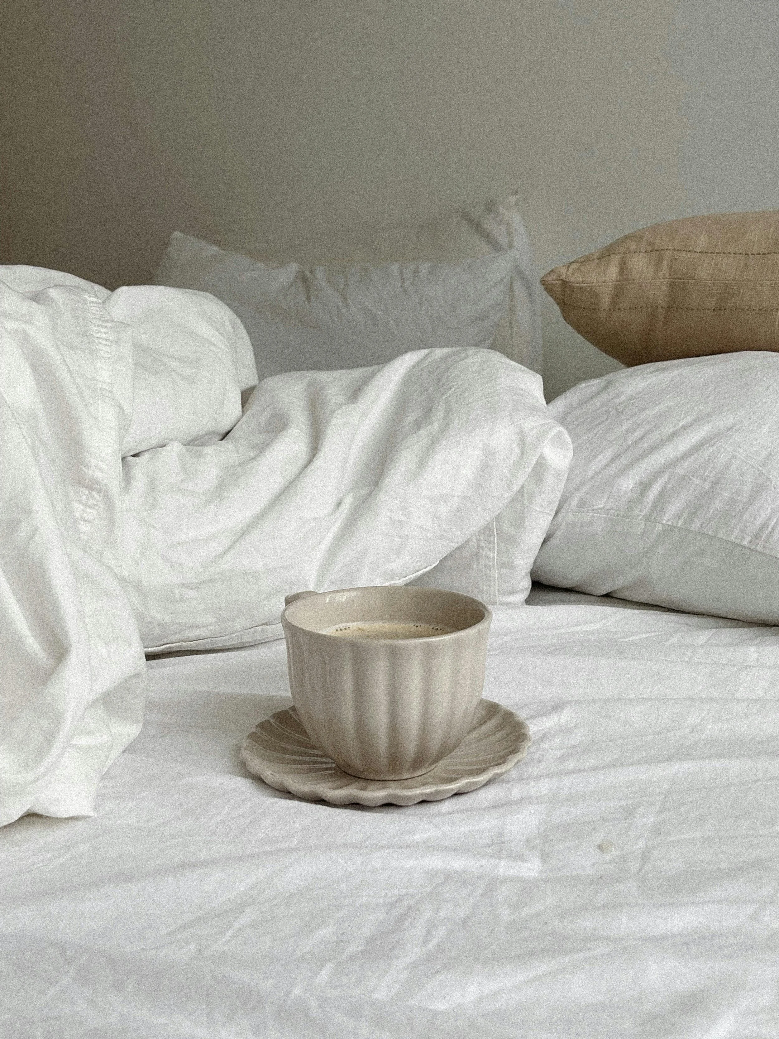 A neutral cup of coffee resting on a rumpled bed, representing a moment of rest and care from stress and burnout