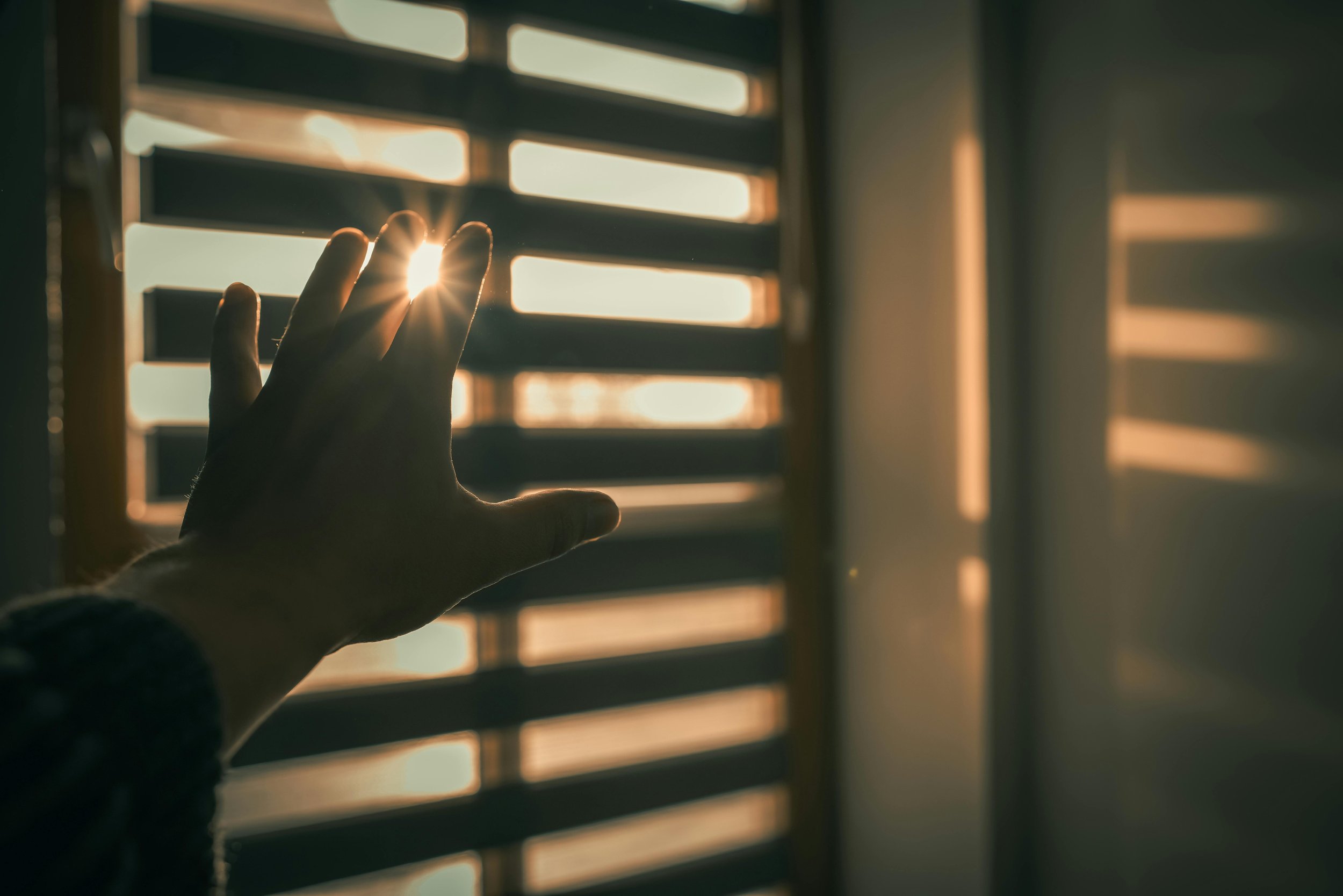 Person reaching toward sunlight through a window, symbolizing seeking relief from stress and burnout.