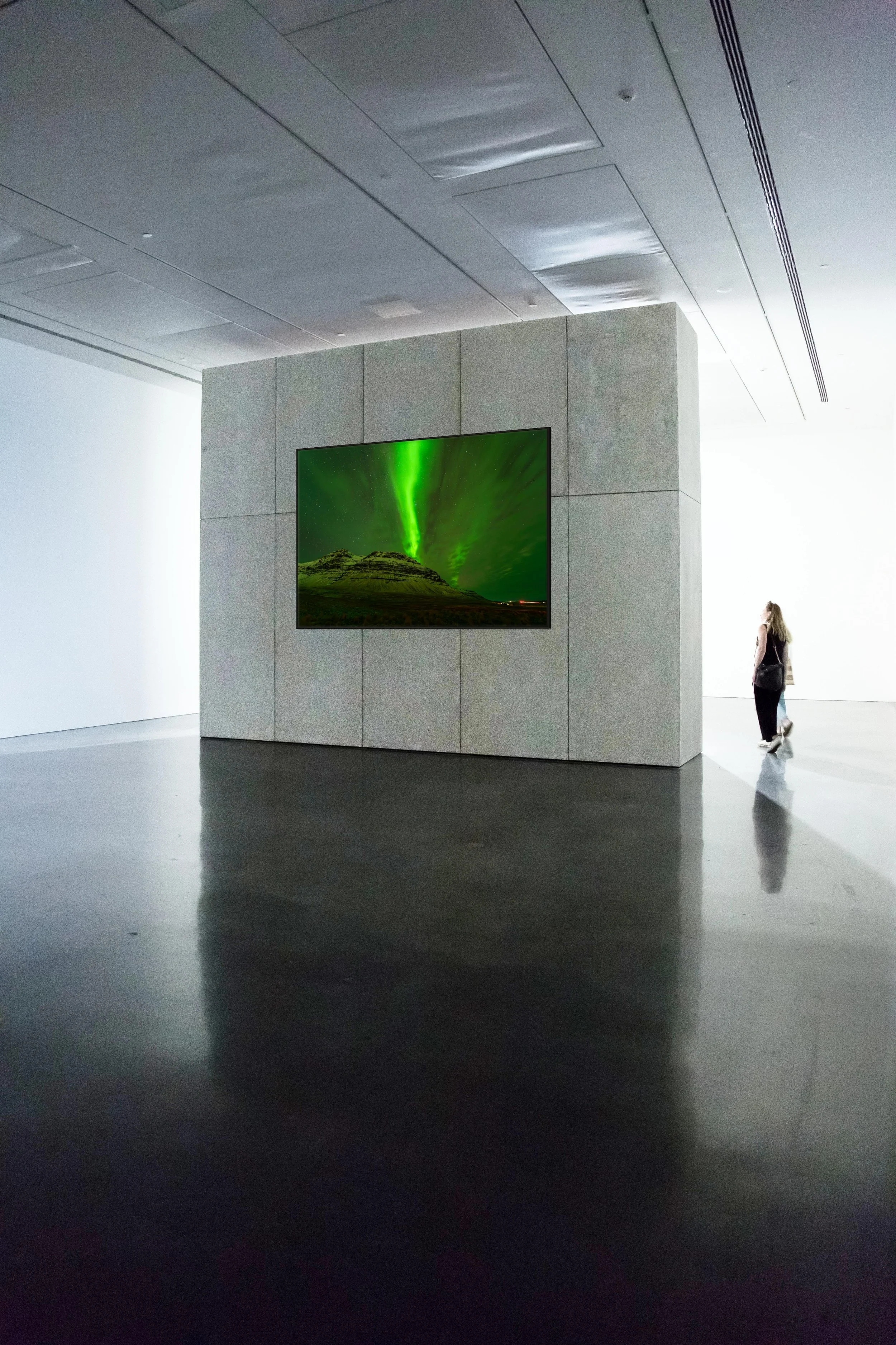 Veil of Light — green aurora over an Iceland peak, framed in black floating wood frame on a freestanding gallery wall in a modern museum with polished concrete floors.