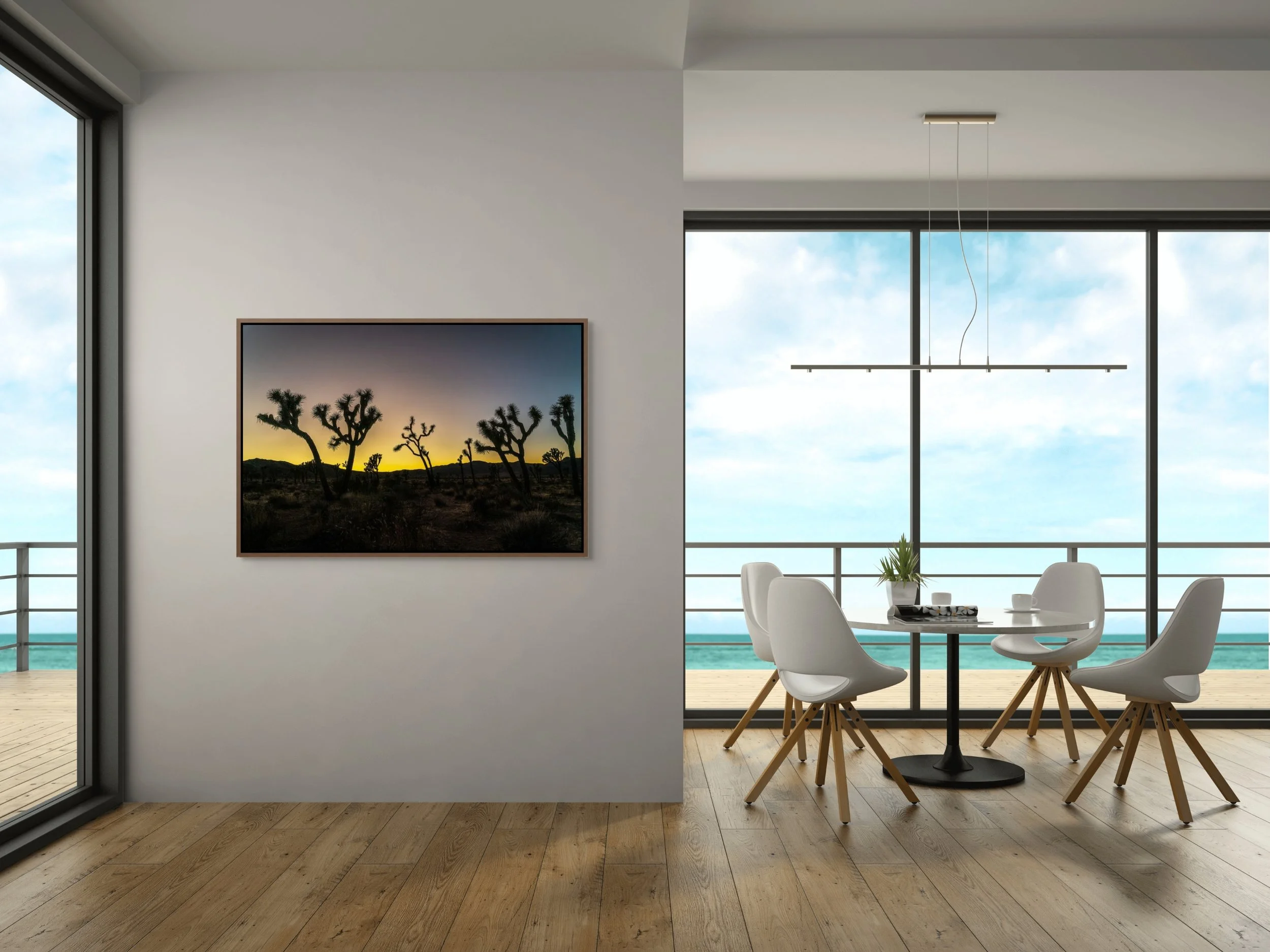 Desert Sentinels — Joshua Tree silhouettes at gold dusk, framed in alder brown floating wood frame, styled in a bright coastal dining nook with floor-to-ceiling windows.