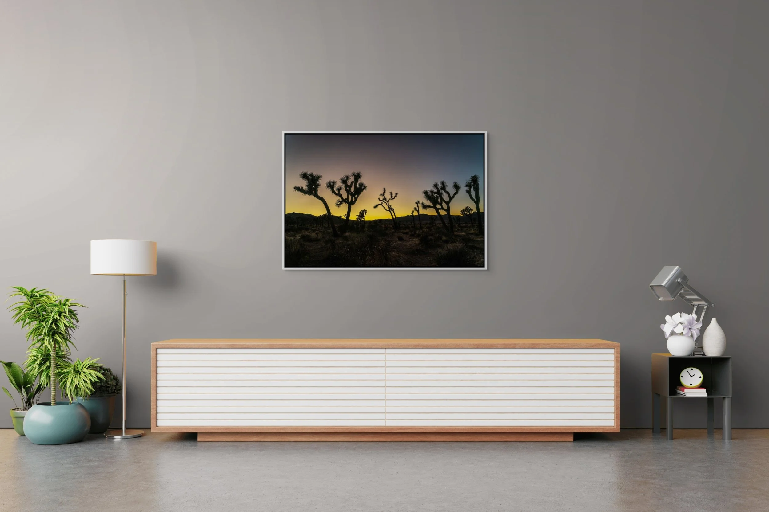 Desert Sentinels — Joshua Tree silhouettes at gold dusk, framed in white floating wood frame, over a minimalist credenza with plant and sculpture.