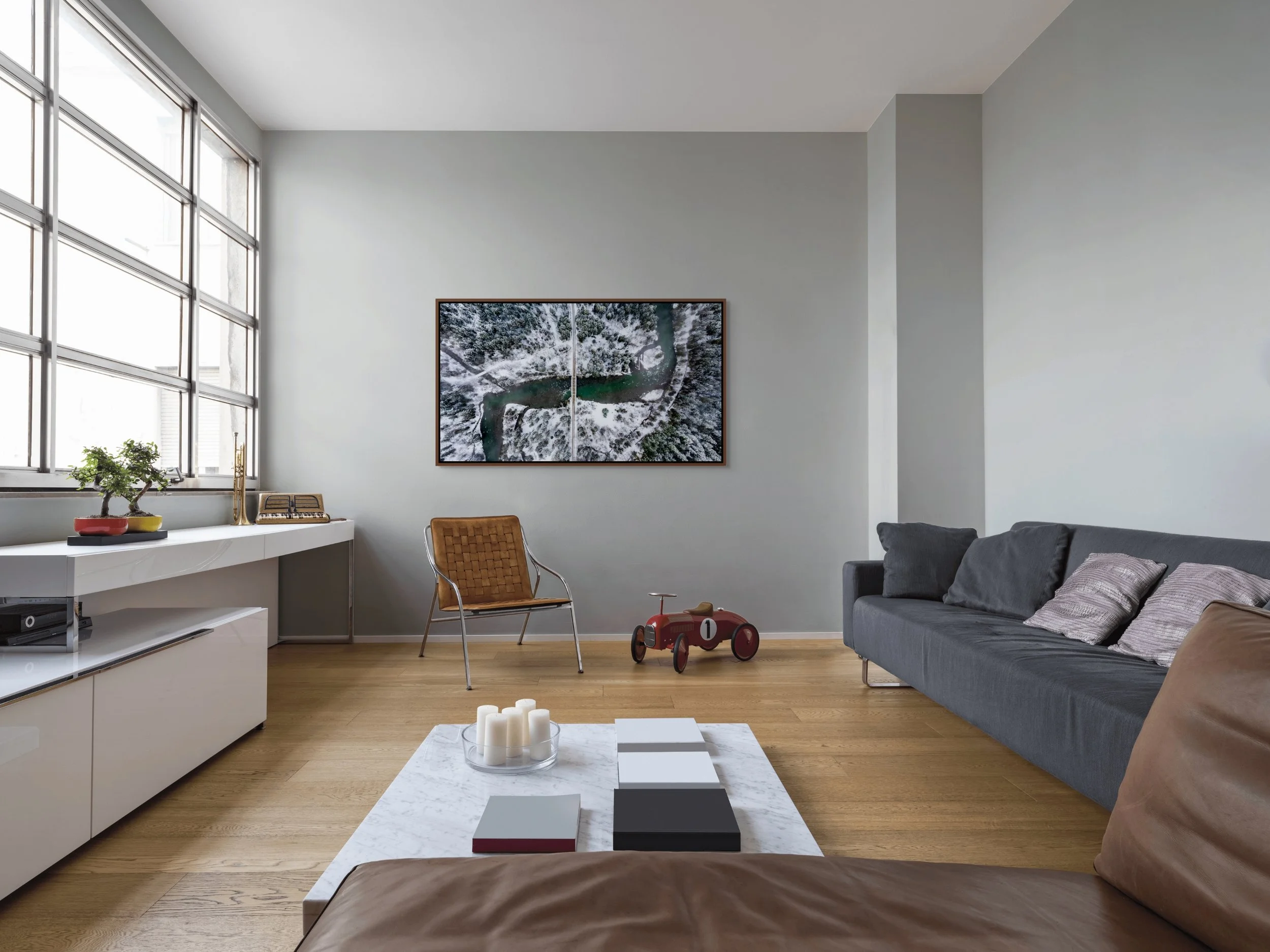 The Hidden Crossing, framed in Alder Brown floating frame, above a tan sofa with floor lamp and plant in a bright living room.