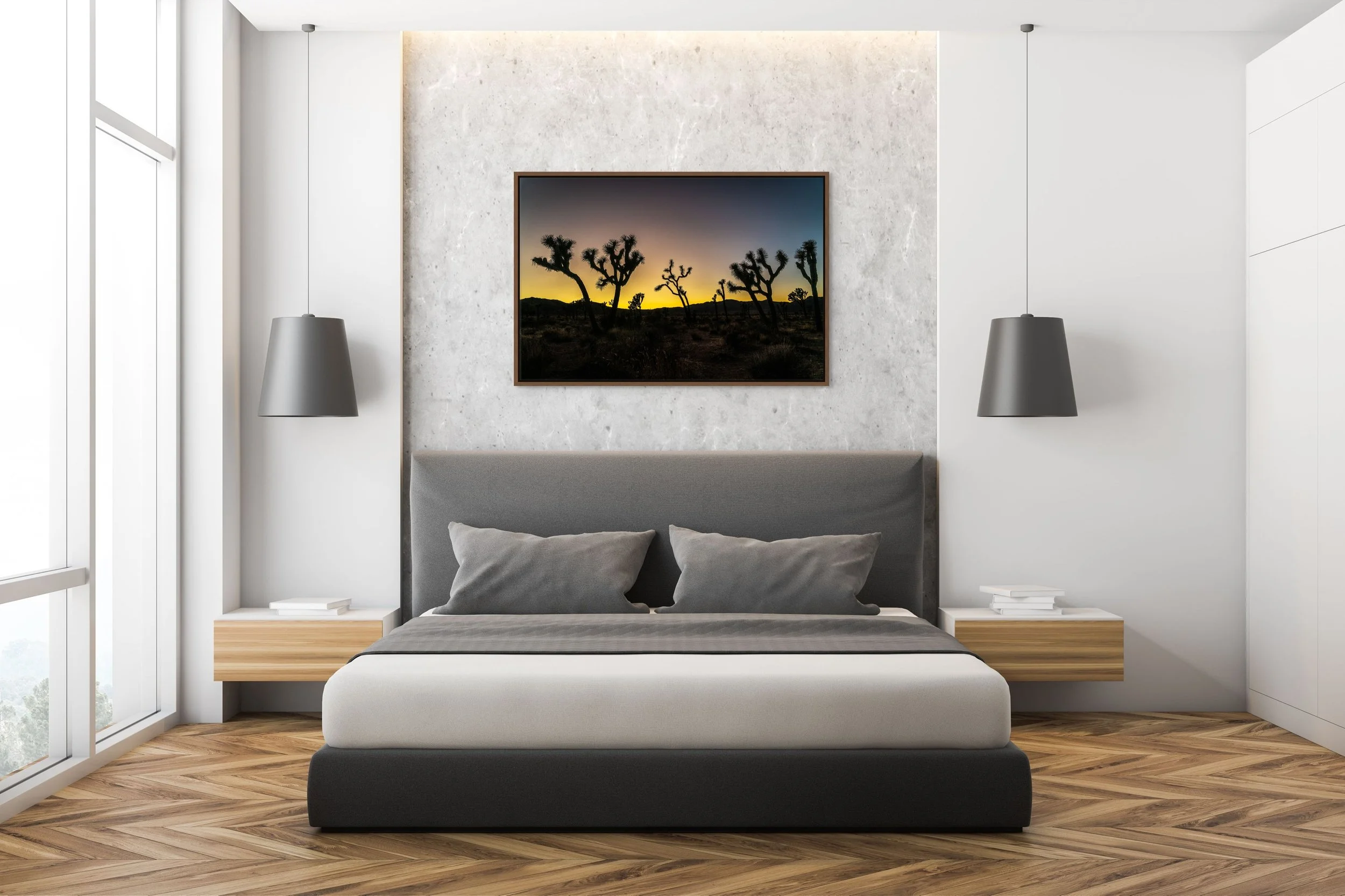 Desert Sentinels — Joshua Tree silhouettes at gold dusk, framed in walnut floating wood frame, above a serene bedroom with an upholstered headboard and pendant lamps.