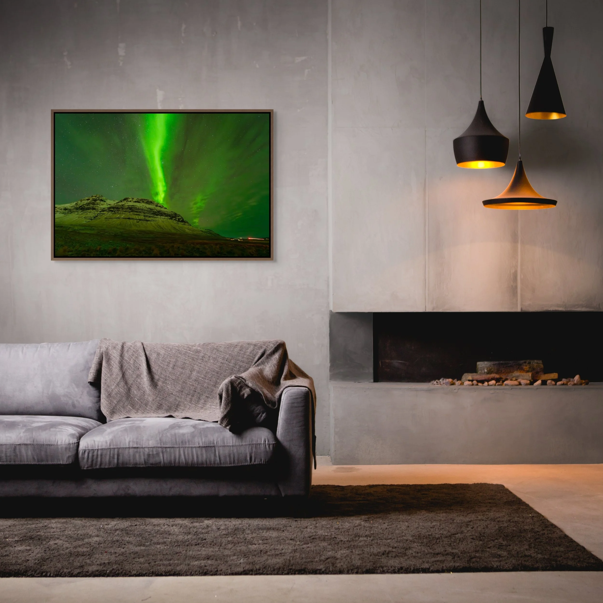 Veil of Light — green aurora over an Iceland peak, framed in walnut floating wood frame above a concrete fireplace with warm pendant lamps and a gray sofa.