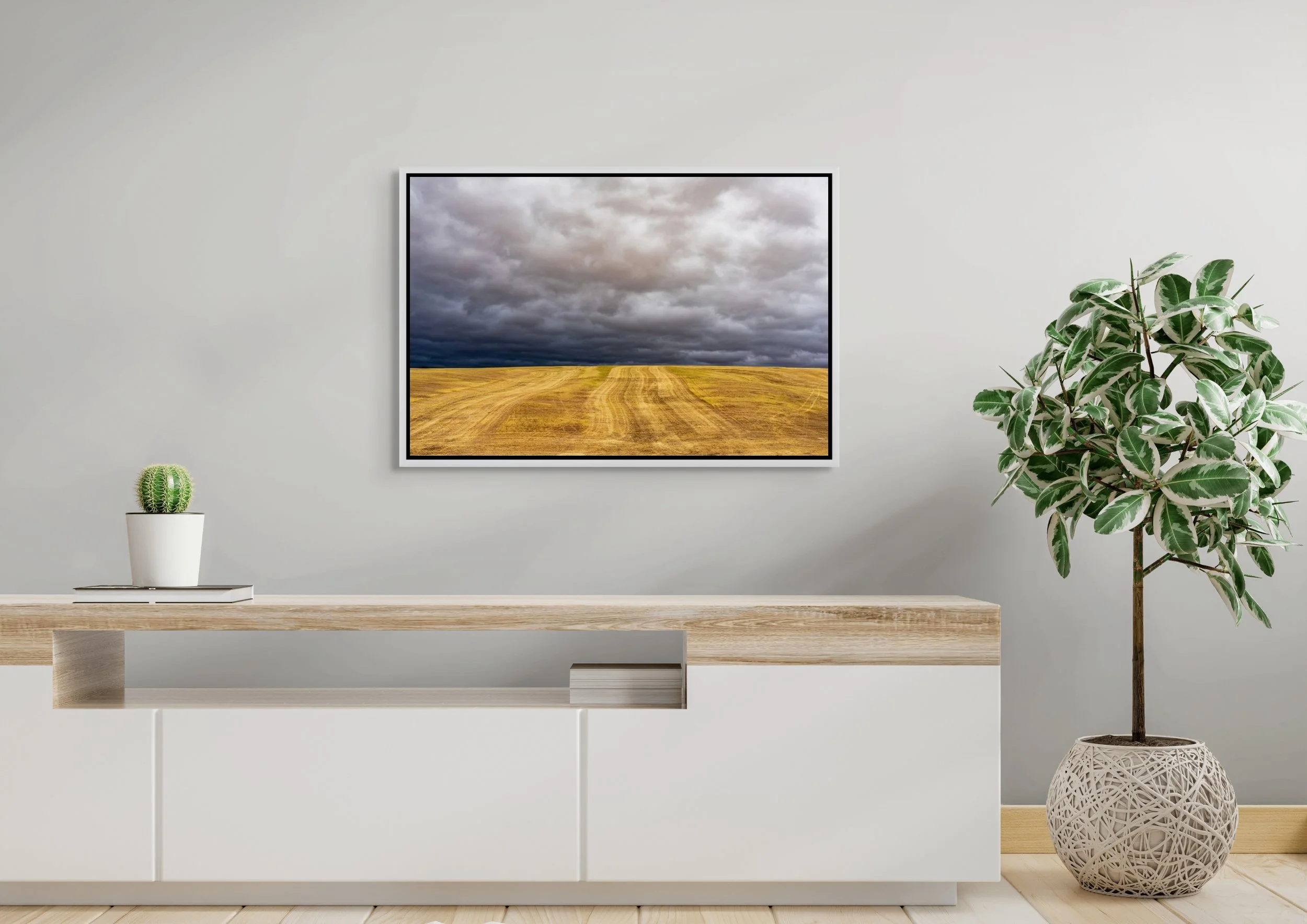 Before the Storm in a floating White frame, mounted above a clean white sideboard with potted greenery.